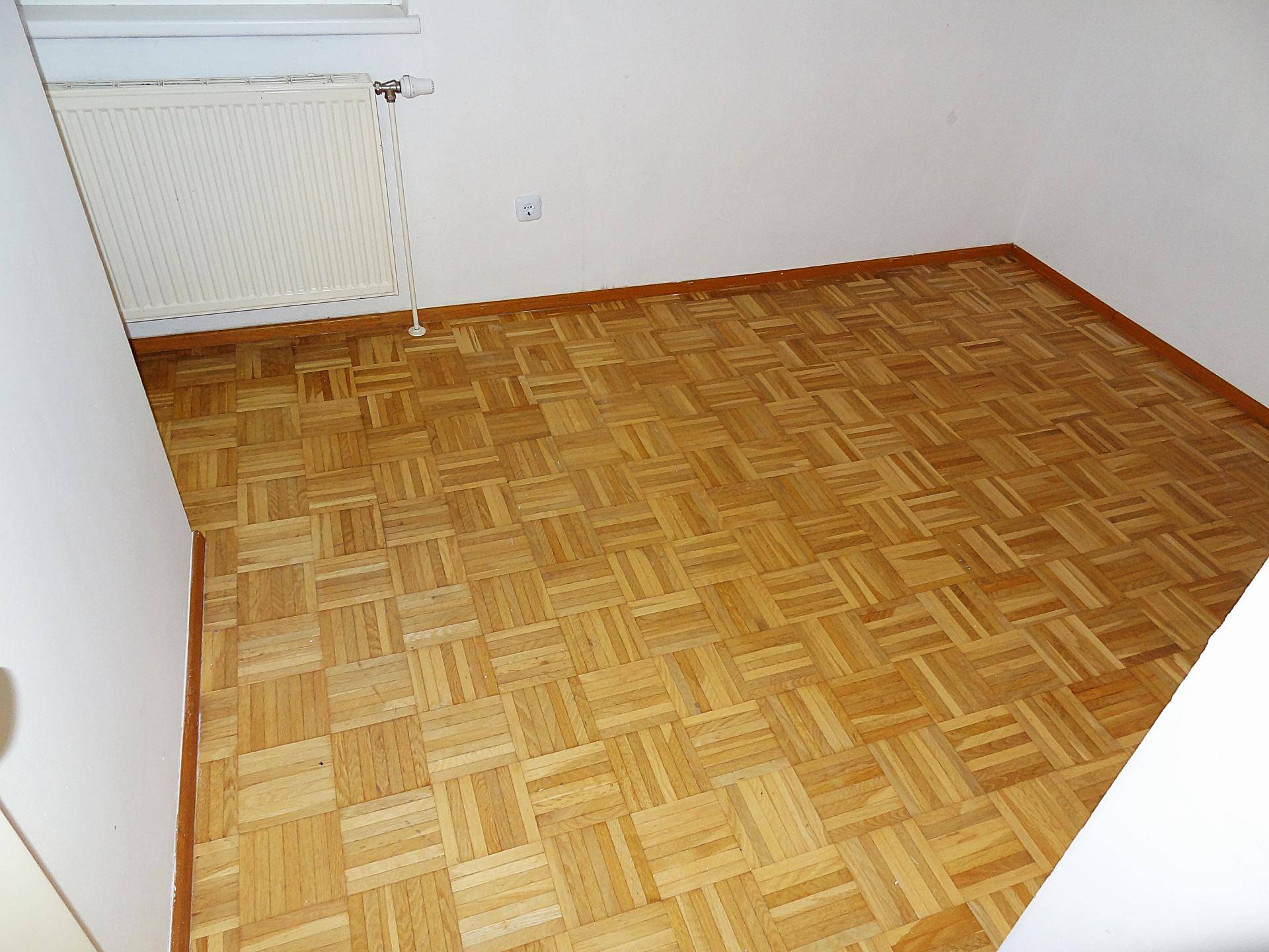 Geräumiges Schlafzimmer mit Parkettboden, weißen Wänden und Heizkörper unter dem Fenster.