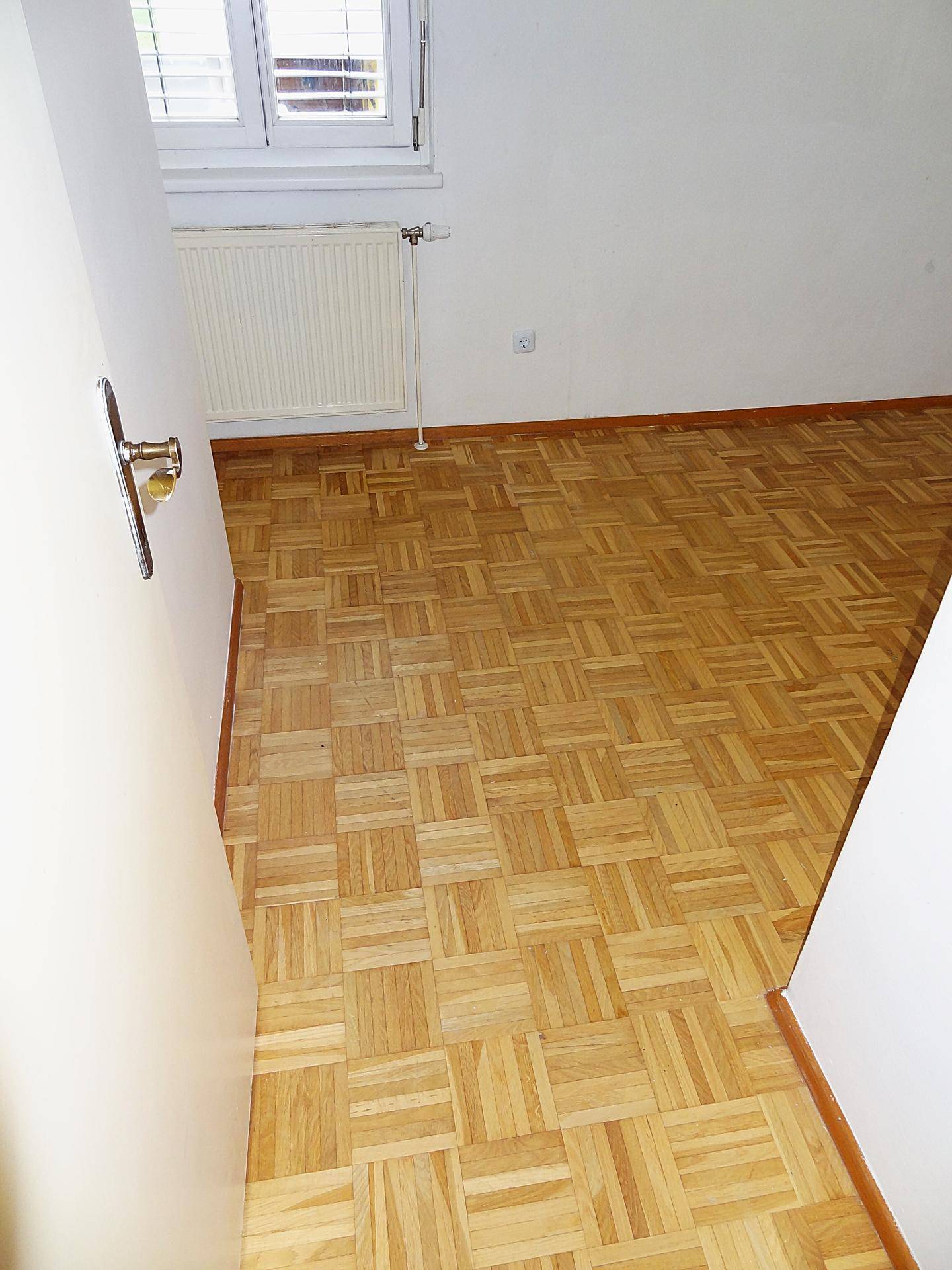Blick durch die Tür in ein helles Schlafzimmer mit Parkettboden und Fenster.