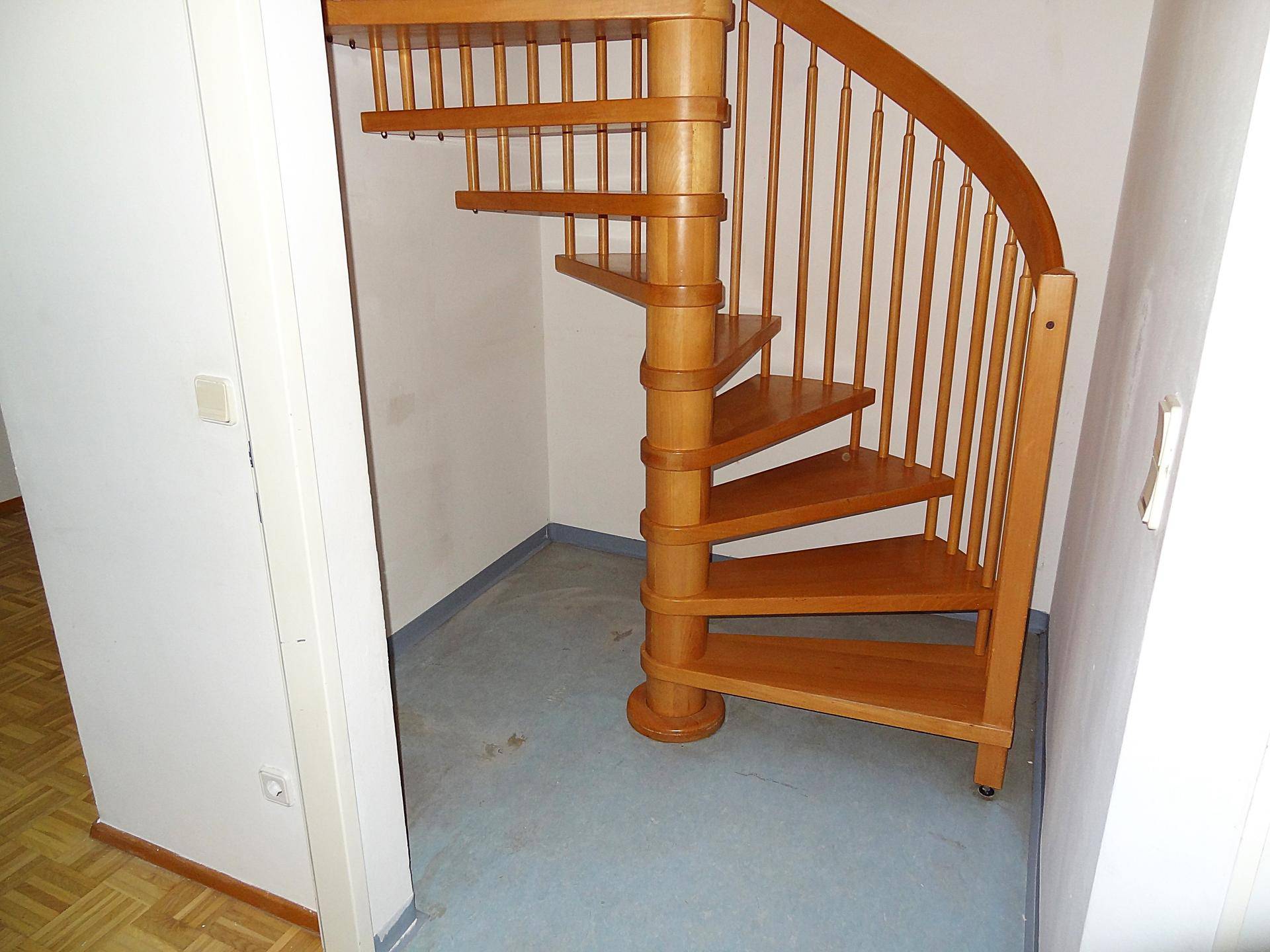 Heller Flur mit einer eleganten Holzwendeltreppe und blauem Bodenbelag.