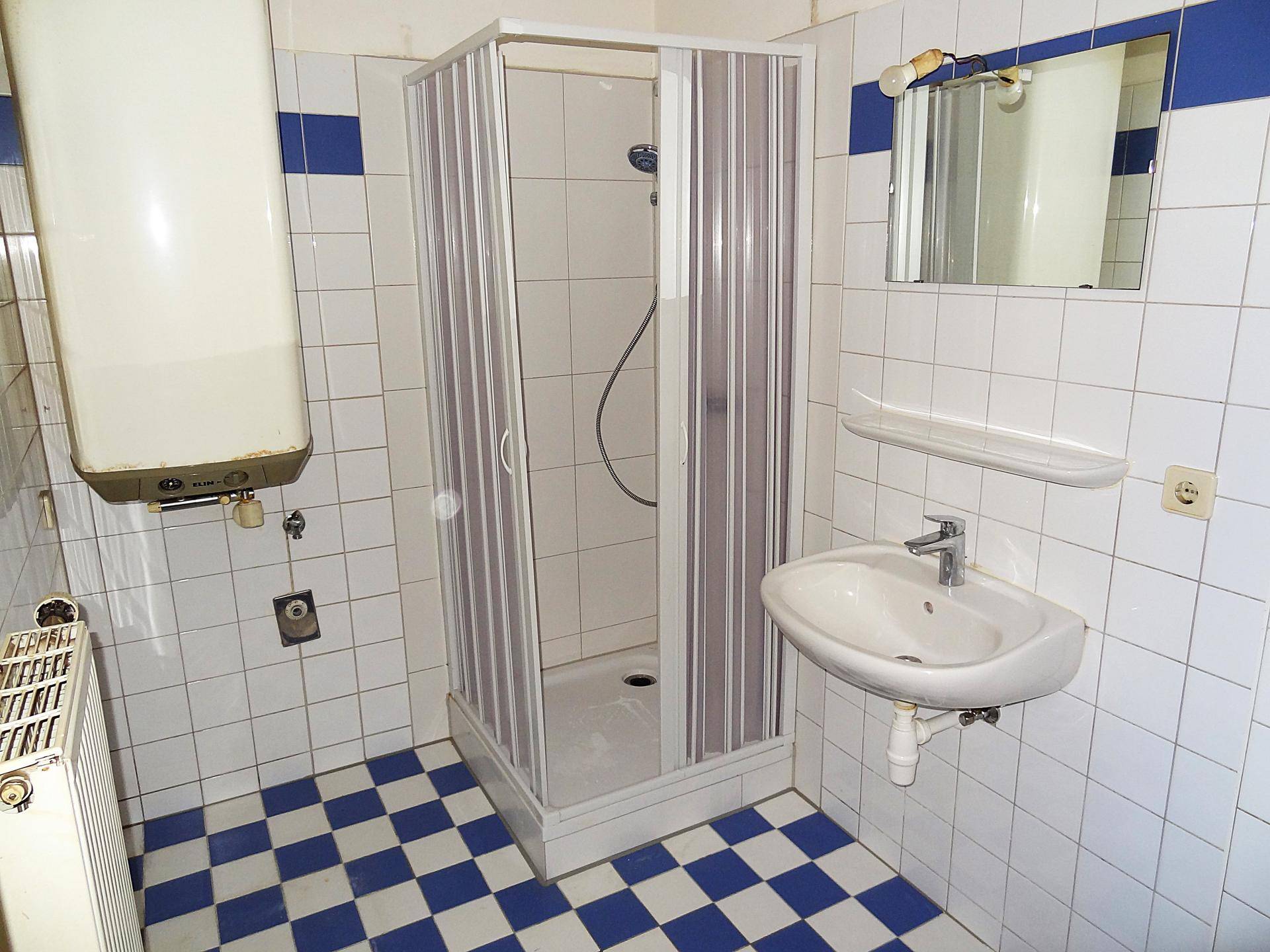 Badezimmer mit Duschkabine, Waschbecken, Toilette und einem Warmwasserboiler an der Wand.