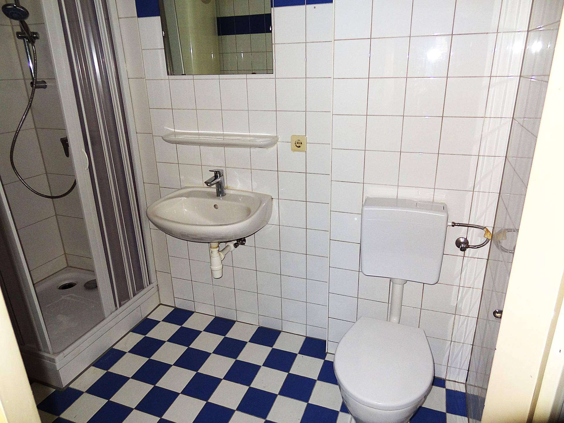 Kompaktes Badezimmer mit Duschkabine, Waschbecken und Toilette, auf kariertem Fliesenboden.