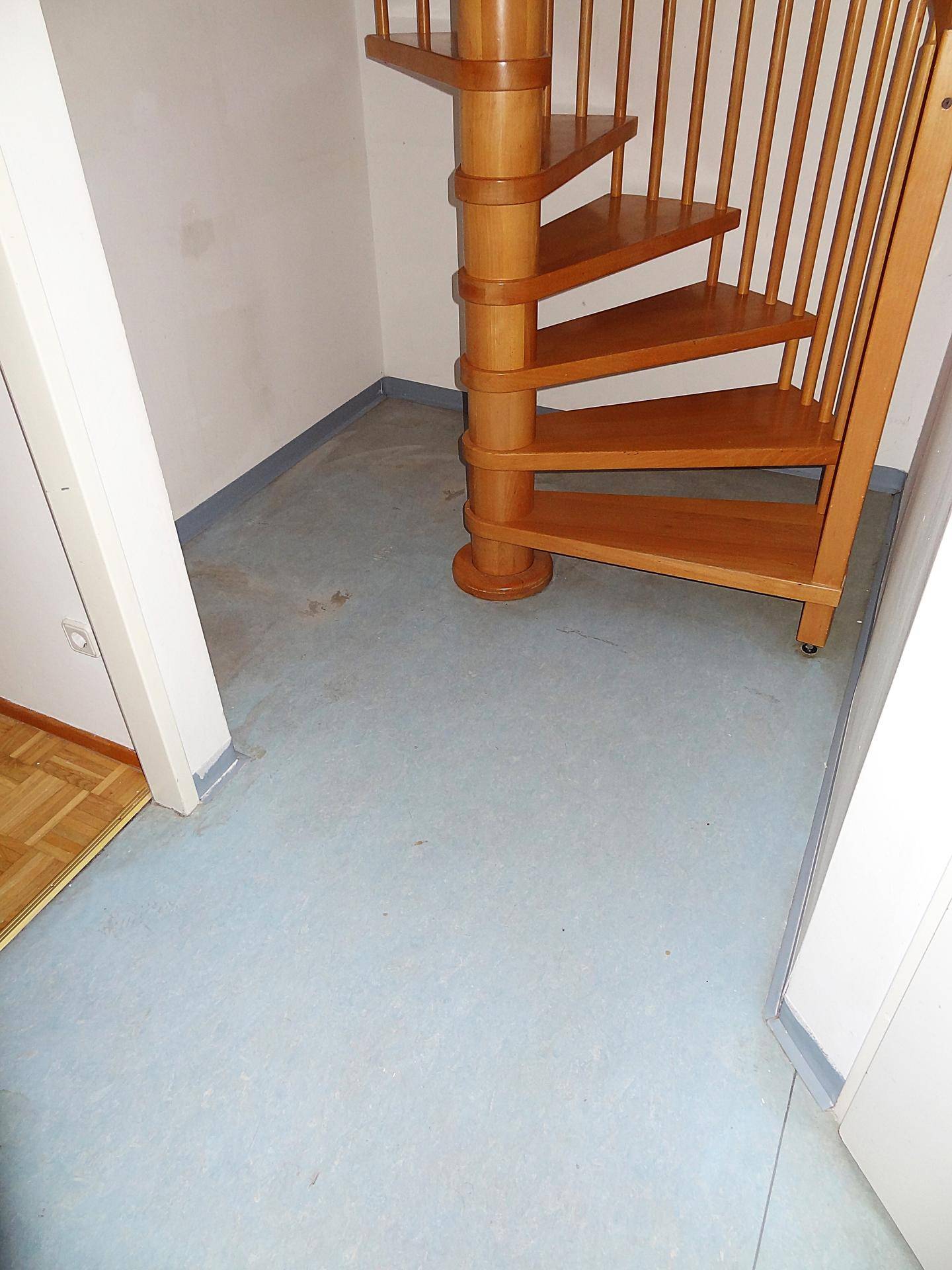 Flur mit blauem Bodenbelag und dem unteren Teil einer Holzwendeltreppe.