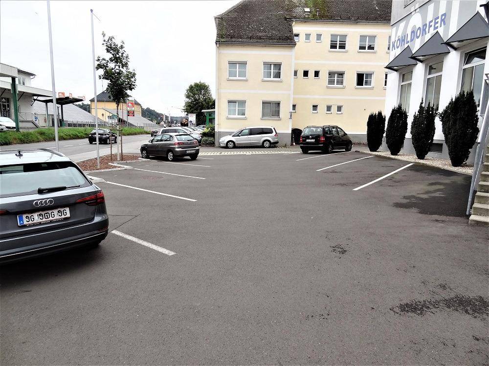 Außenansicht eines Parkplatzes vor einem Gebäude mit mehreren geparkten Autos.