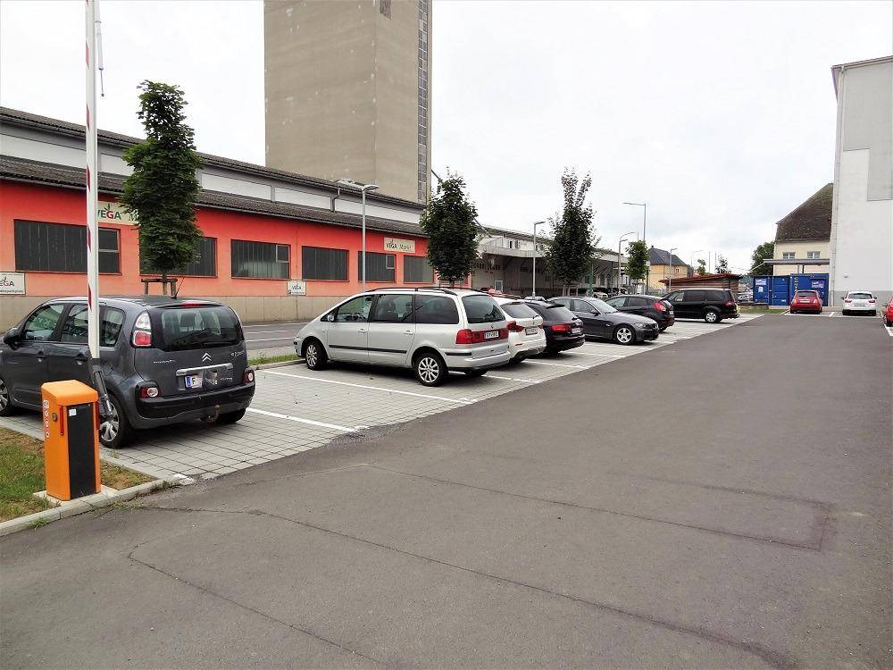 Parkplatz mit geparkten Fahrzeugen und einem roten Gebäude im Hintergrund.