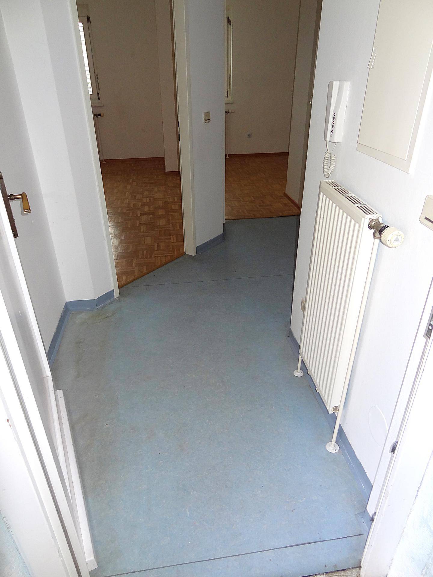 Heller Flur mit blauem Bodenbelag und Blick auf angrenzende Zimmer mit Parkett.