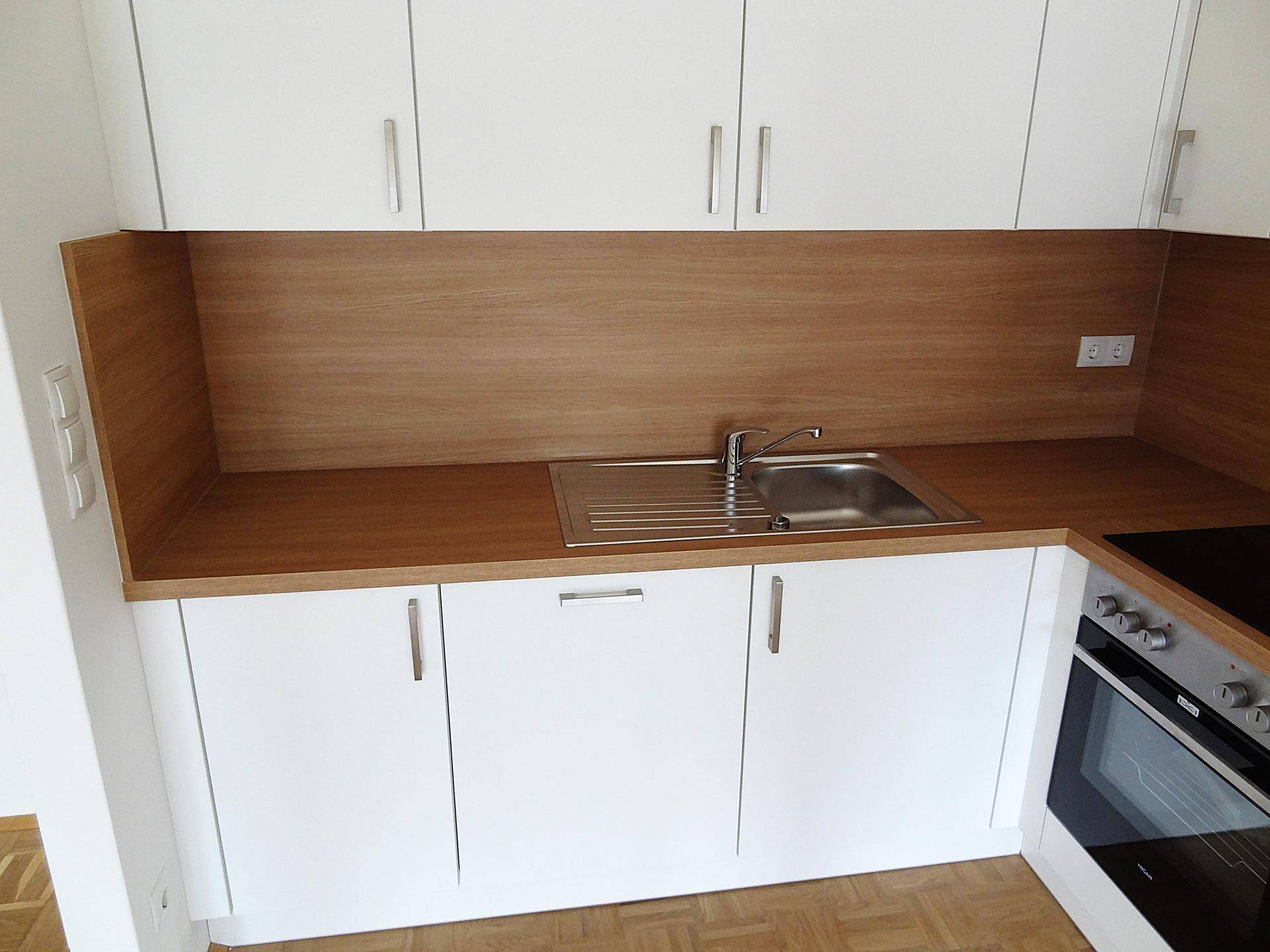 Nahaufnahme des Spülbereichs in der Küche mit Holzrückwand und weißen Schränken.