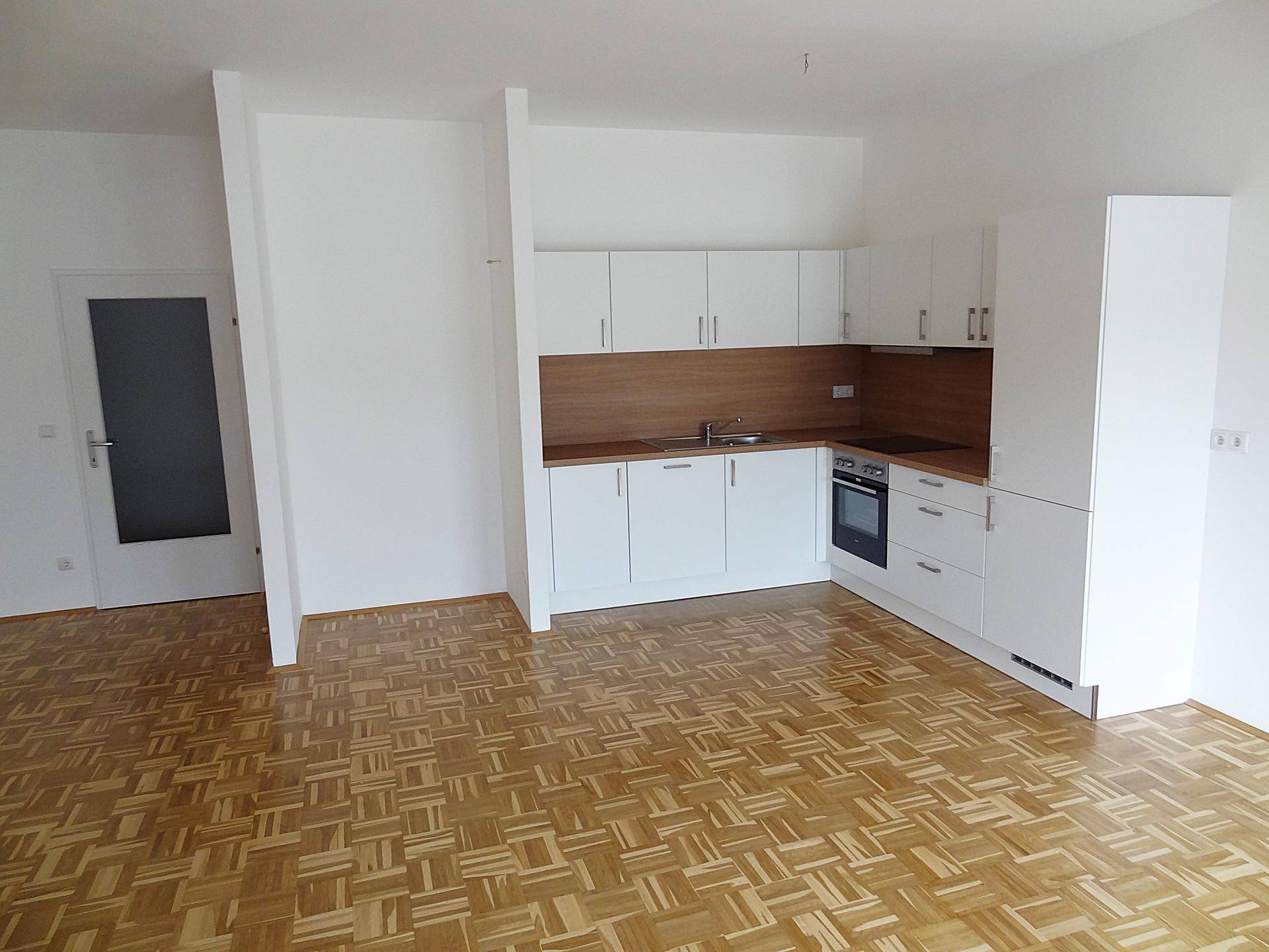 Heller Wohnraum mit offener Küche und einer Tür, die zu einem weiteren Zimmer führt.