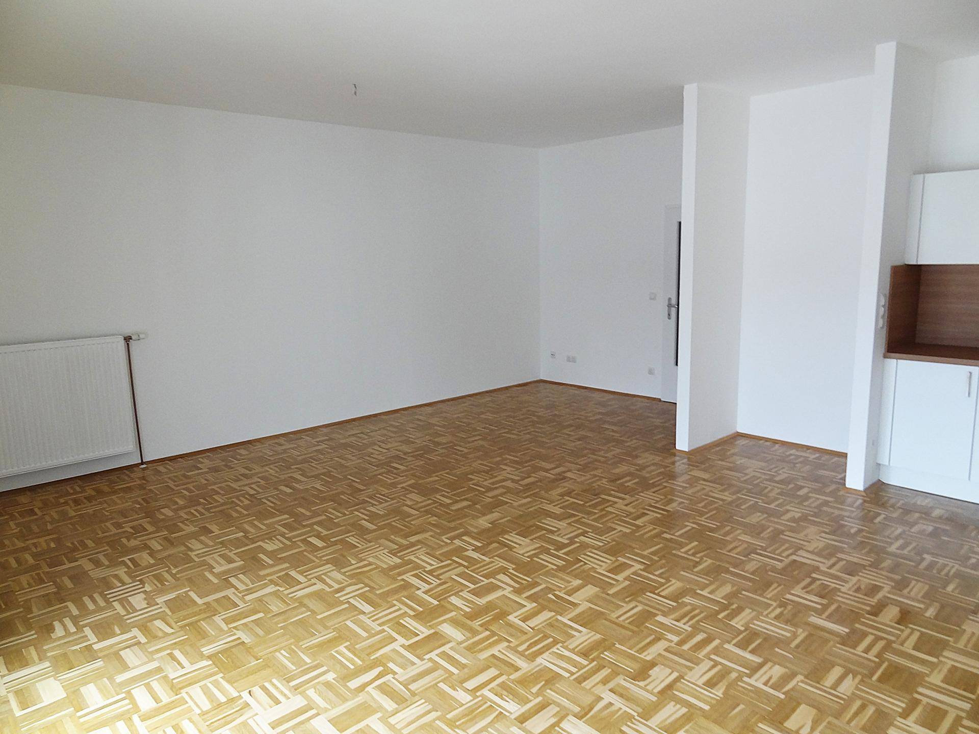 Heller Wohnraum mit Parkettboden und einem Heizkörper an der weißen Wand.