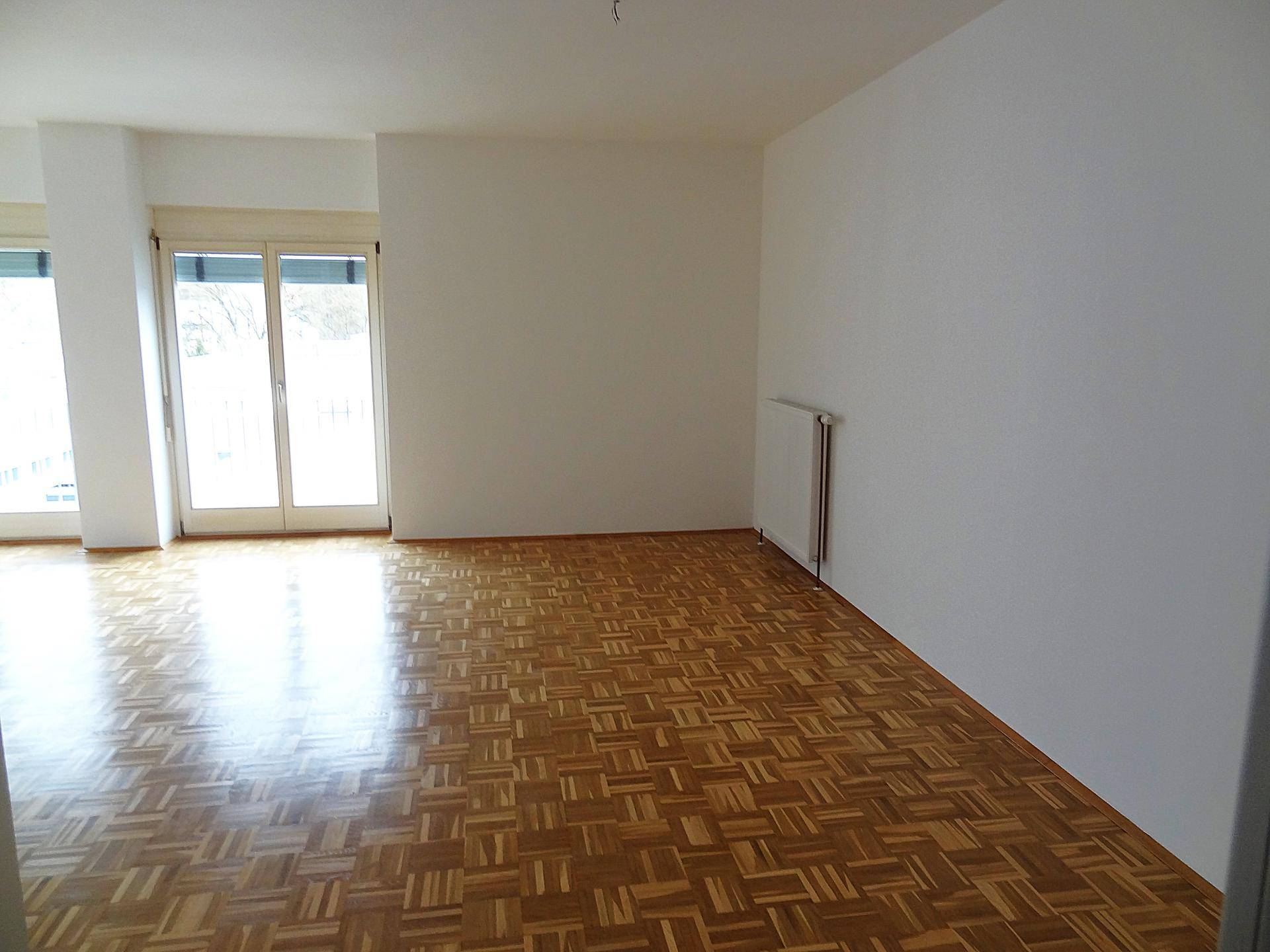 Heller Wohnbereich mit Parkettboden, großem Fenster und einem Heizkörper an der Wand.