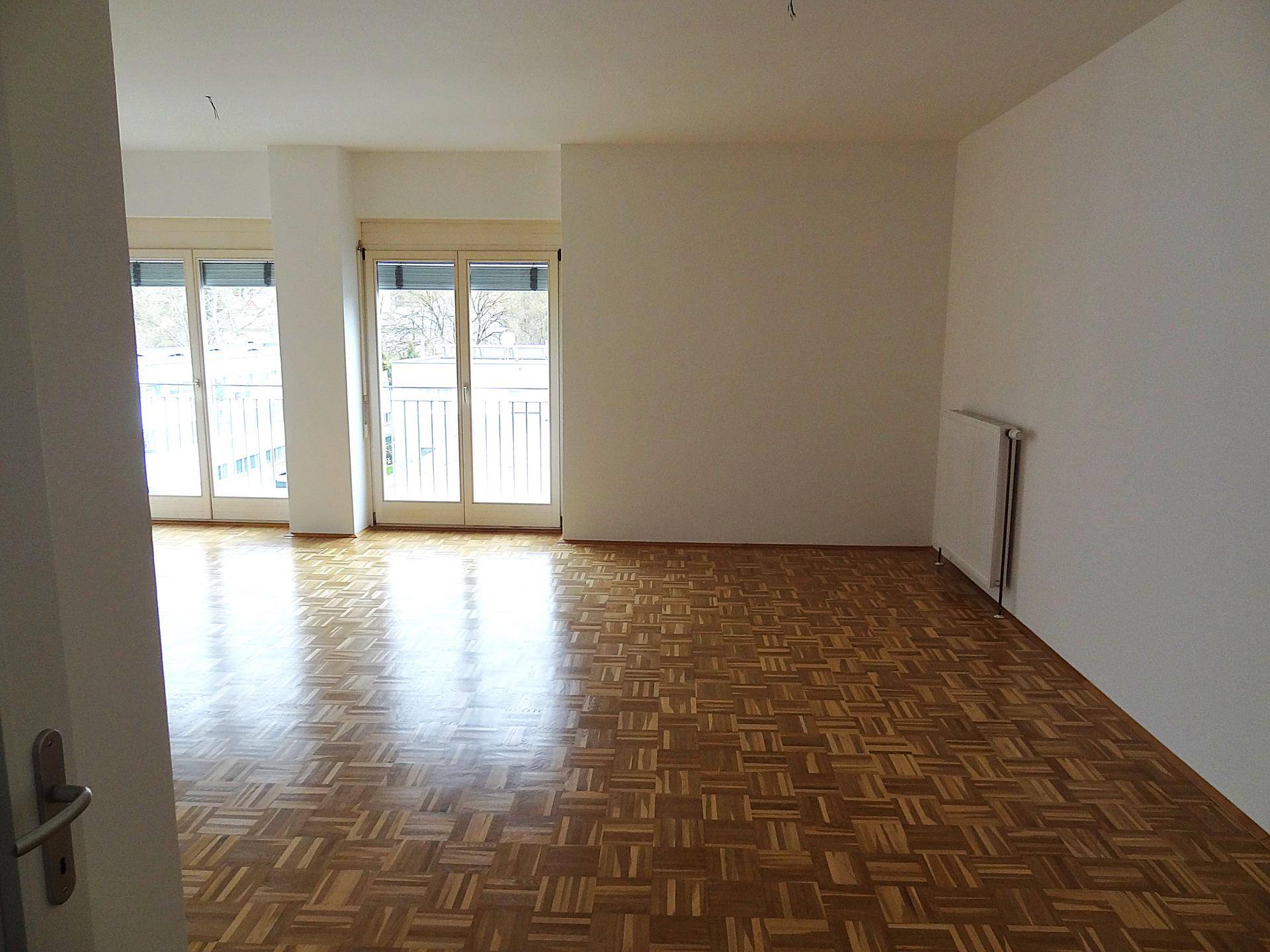 Geräumiger Wohnraum mit Parkettboden, viel Tageslicht und Zugang zu einem Außenbereich.