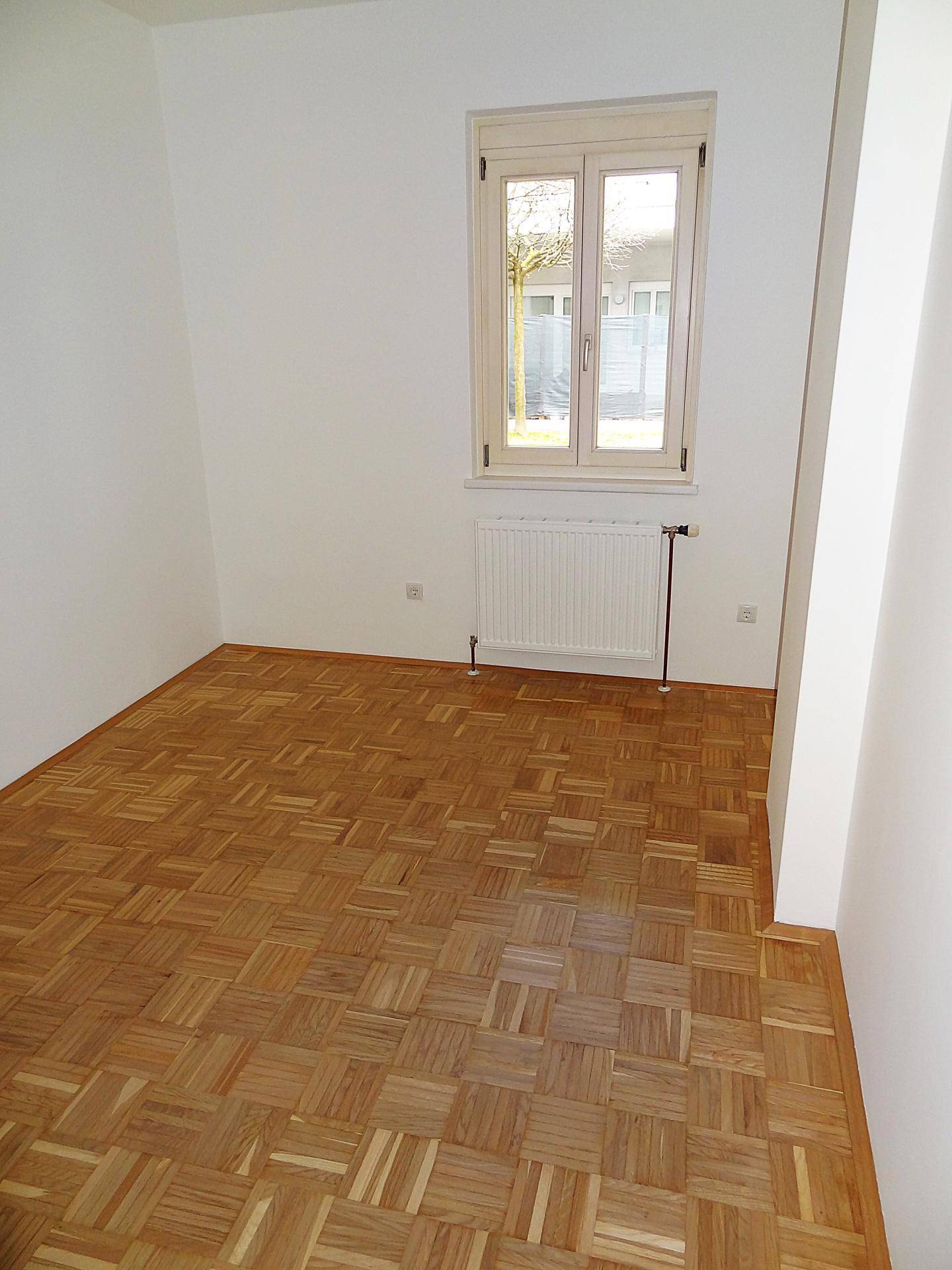 Freundliches Zimmer mit Parkettboden und Fenster, das einen Blick ins Grüne bietet.