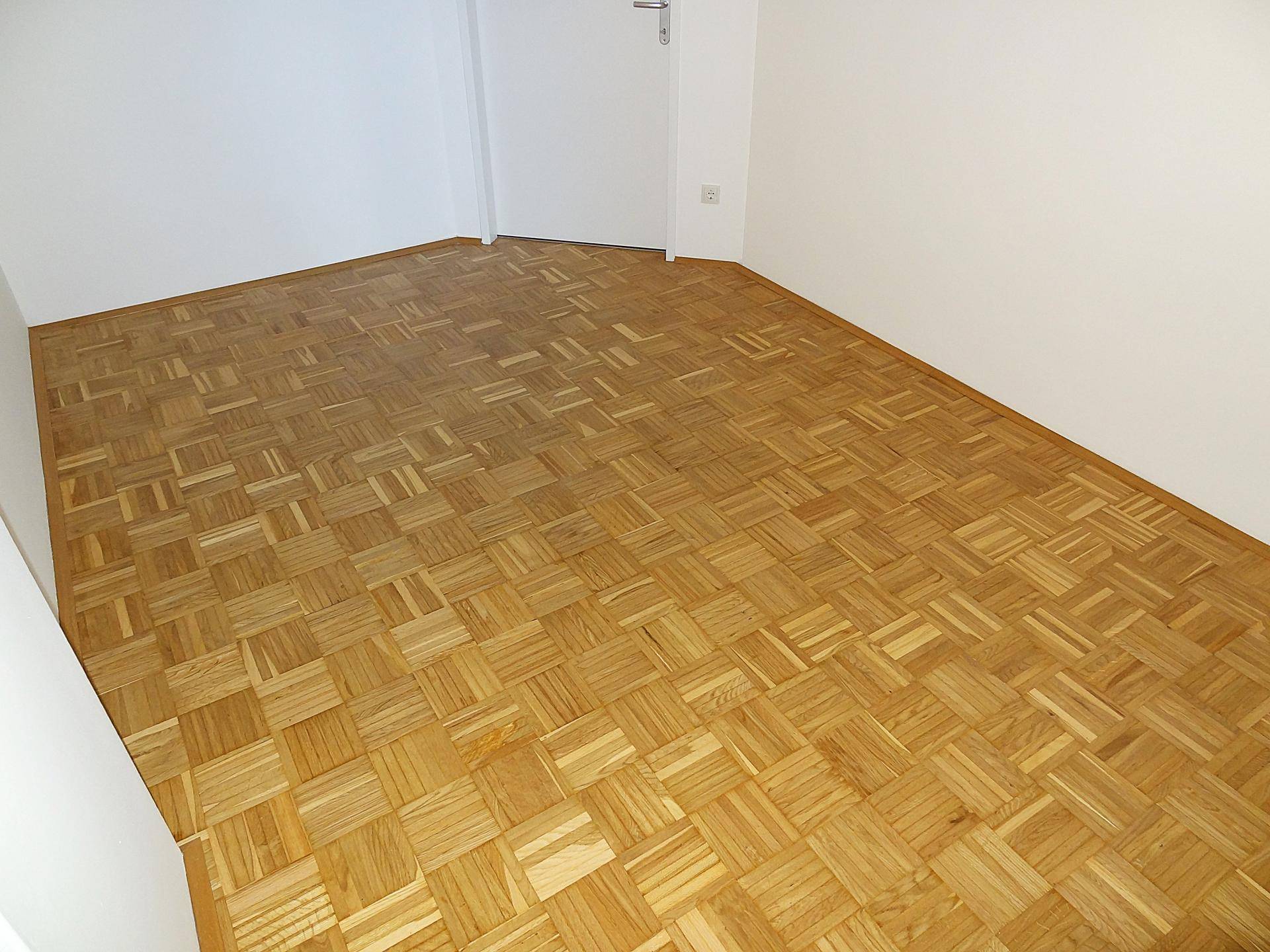 Leeres Zimmer mit Parkettboden und weißen Wänden, bereit für neue Bewohner.