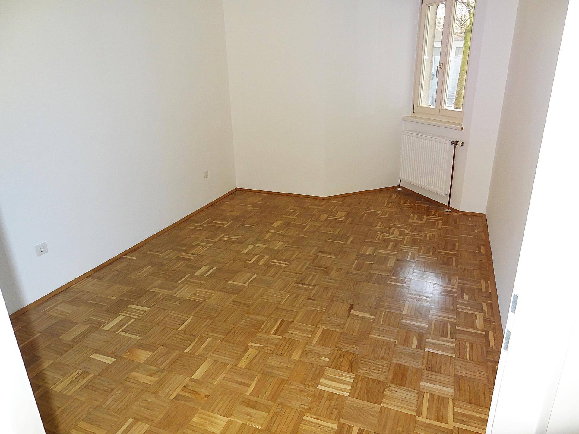 Helles Zimmer mit Parkettboden und Fenster, das für eine angenehme Wohnatmosphäre sorgt.