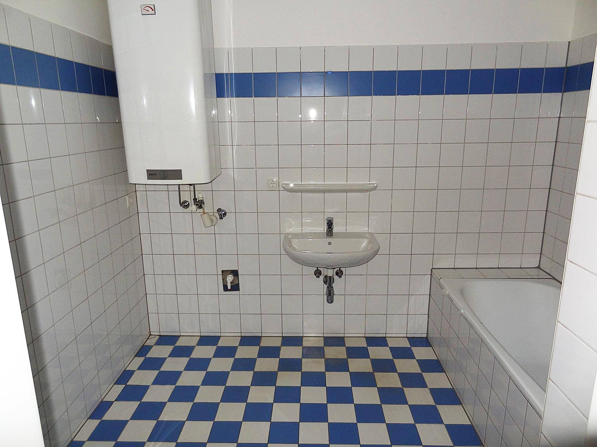 Badezimmer mit blau-weiß kariertem Fliesenboden, Badewanne, Waschbecken und Warmwasserboiler.