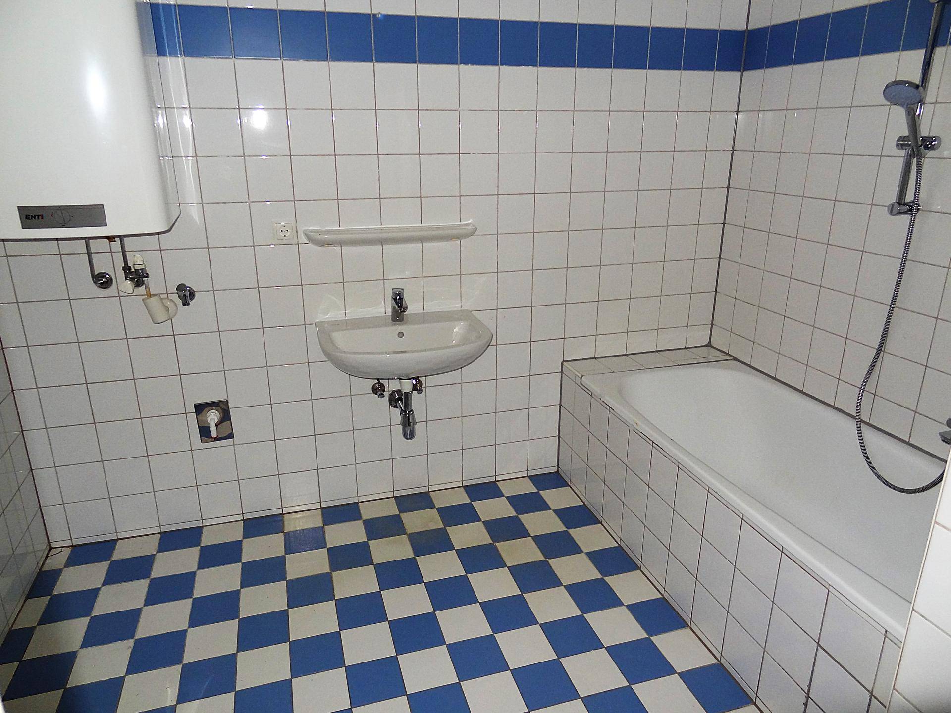 Badezimmer mit Badewanne inklusive Duschfunktion, Waschbecken und blau-weißen Fliesen.