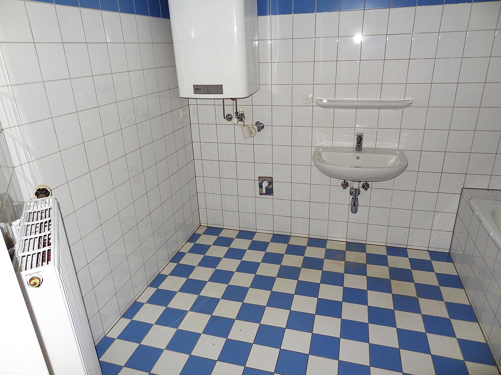 Badezimmer mit Badewanne, Waschbecken, Warmwasserboiler und einem Heizkörper.