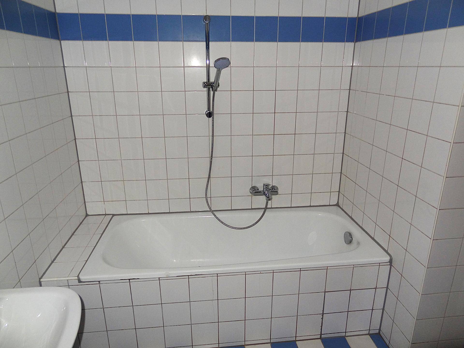 Badewanne mit Duscharmatur und weiß-blauen Fliesen, bereit für den täglichen Gebrauch.