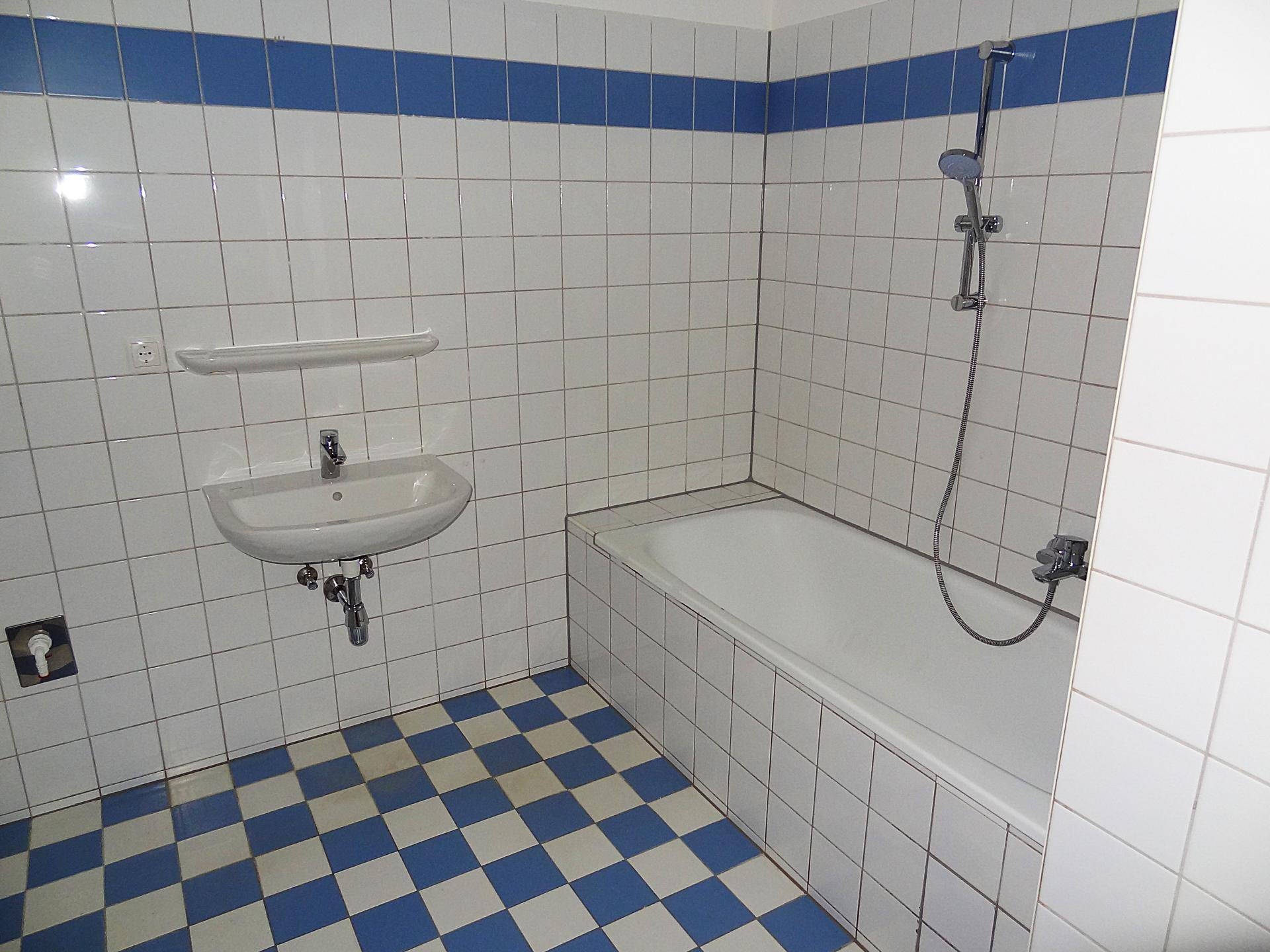 Badezimmer mit Badewanne, Waschbecken und blau-weißen Fliesen, bietet grundlegende Ausstattung.