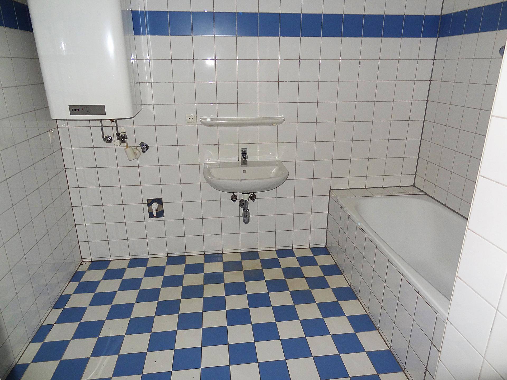 Badezimmer mit Badewanne, Waschbecken und Warmwasserboiler, ausgestattet mit blau-weißen Fliesen.