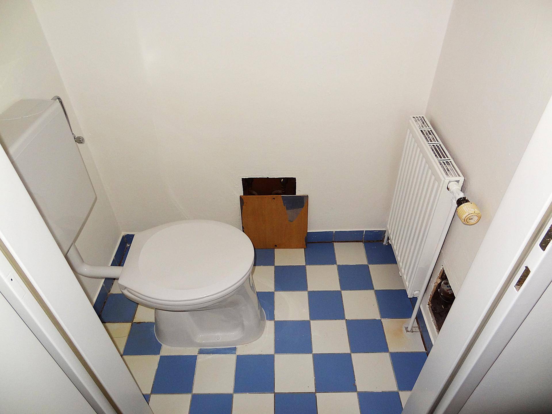 Kleiner Toilettenraum mit blau-weiß kariertem Fliesenboden und einem Heizkörper an der Wand.