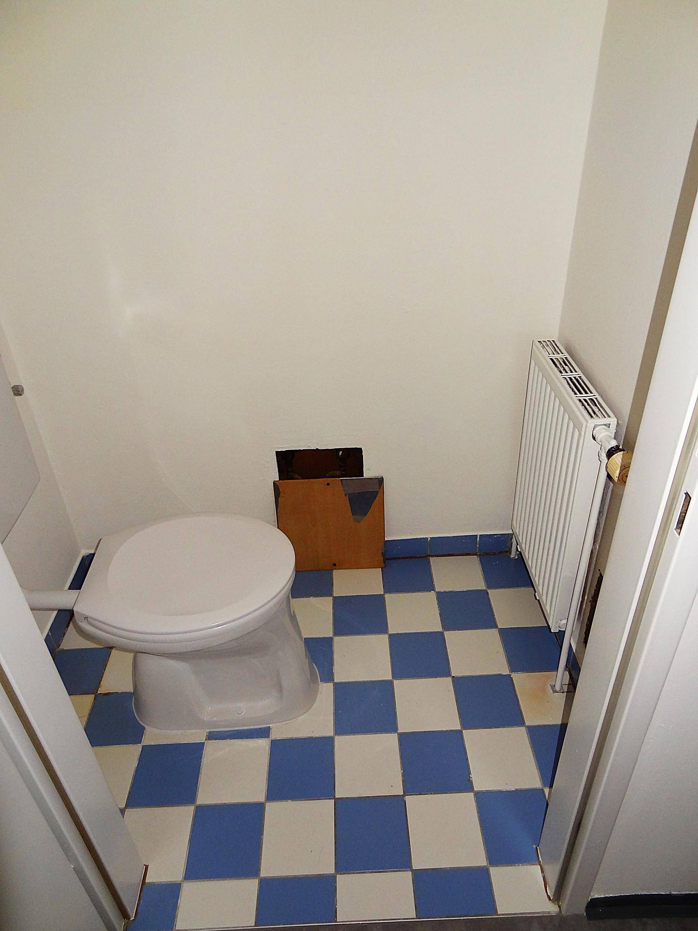 Kleines separates WC mit Steh-WC, Heizkörper und blau-weiß kariertem Fliesenboden.