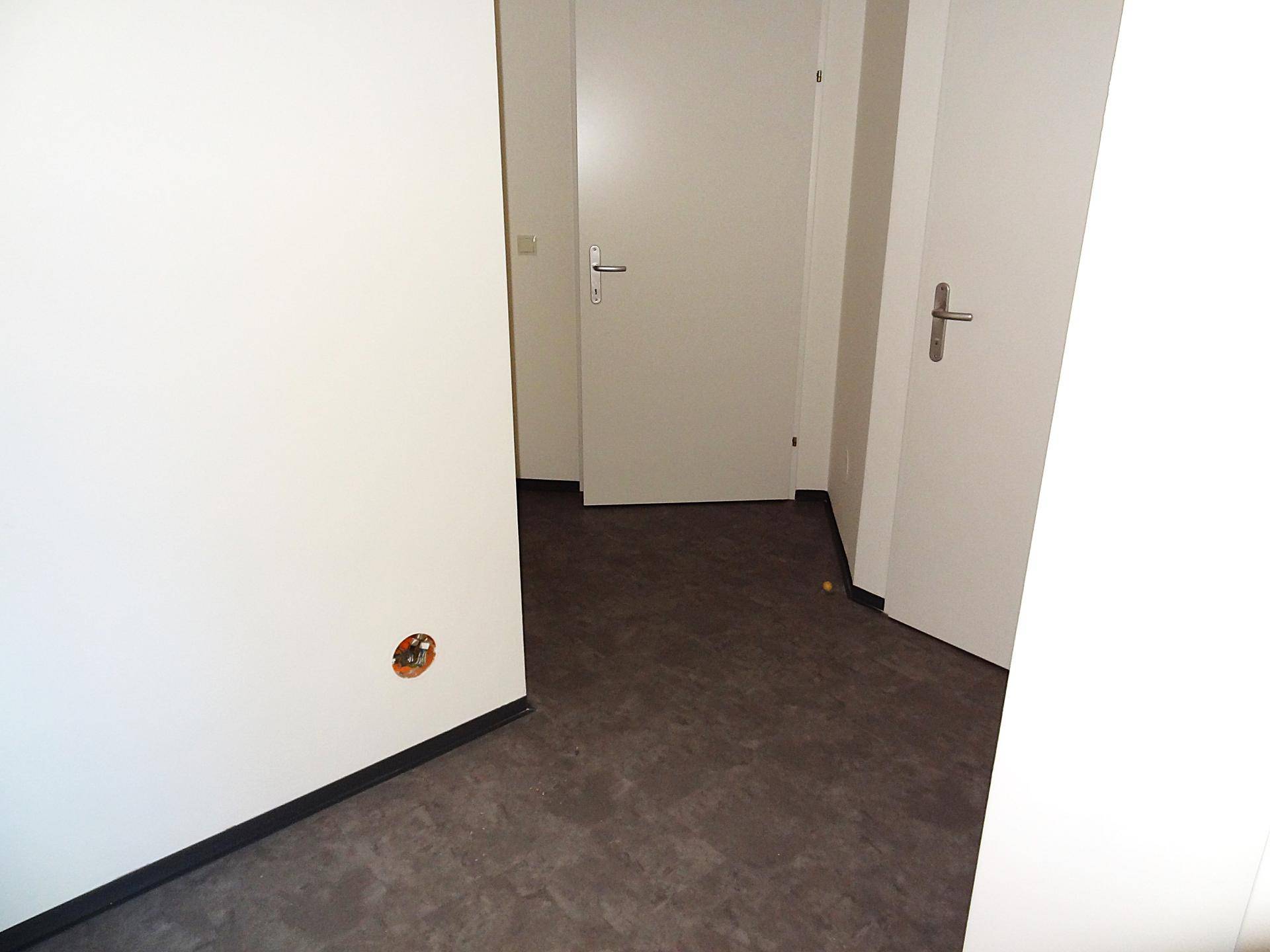 Ecke eines hellen Flurs mit grauem Bodenbelag und weißen Türen, die zu den Zimmern führen.