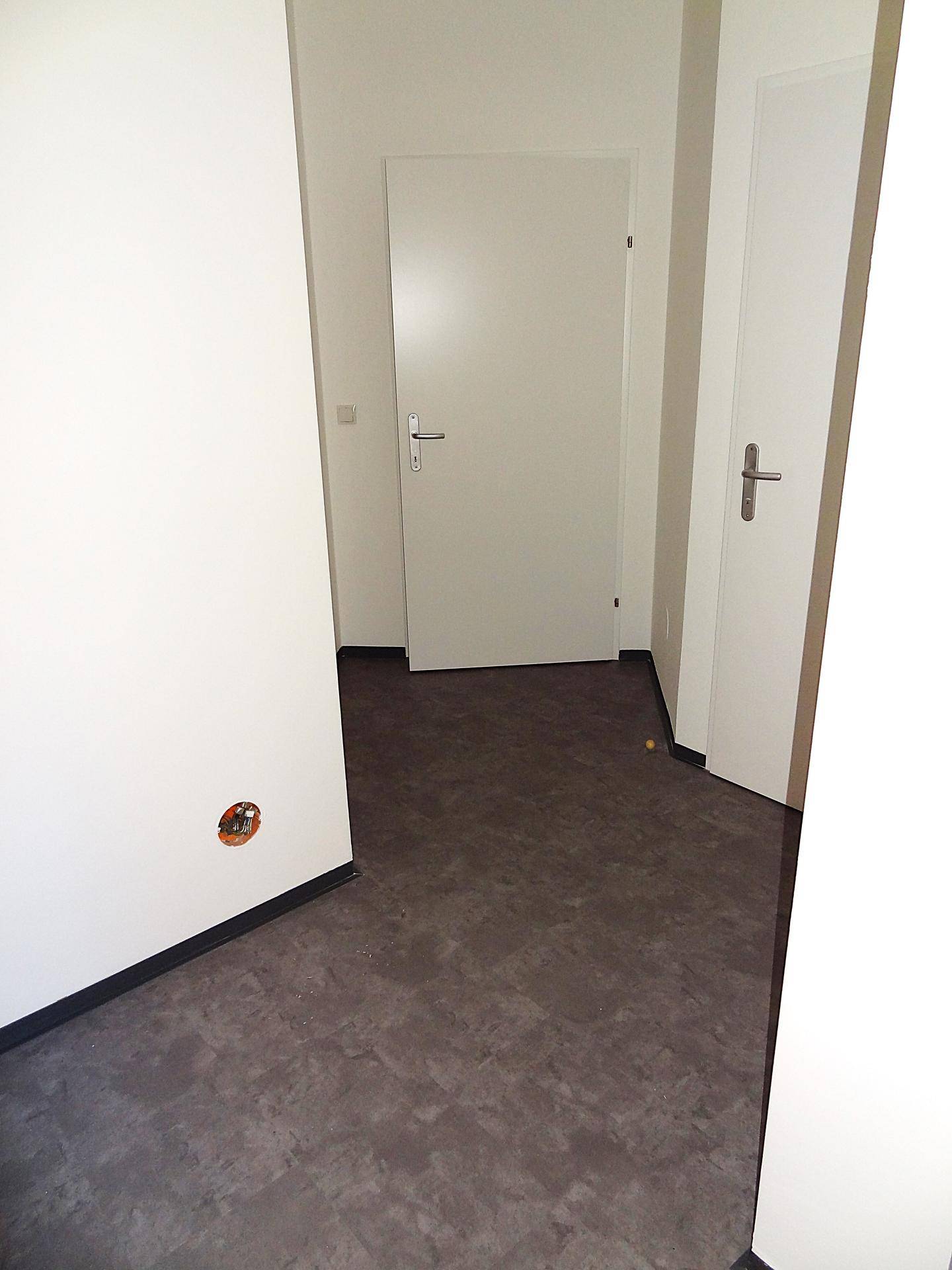 Geräumiger Flur mit grauem Bodenbelag und weißen Wänden, der den Zugang zu verschiedenen Räumen ermöglicht.