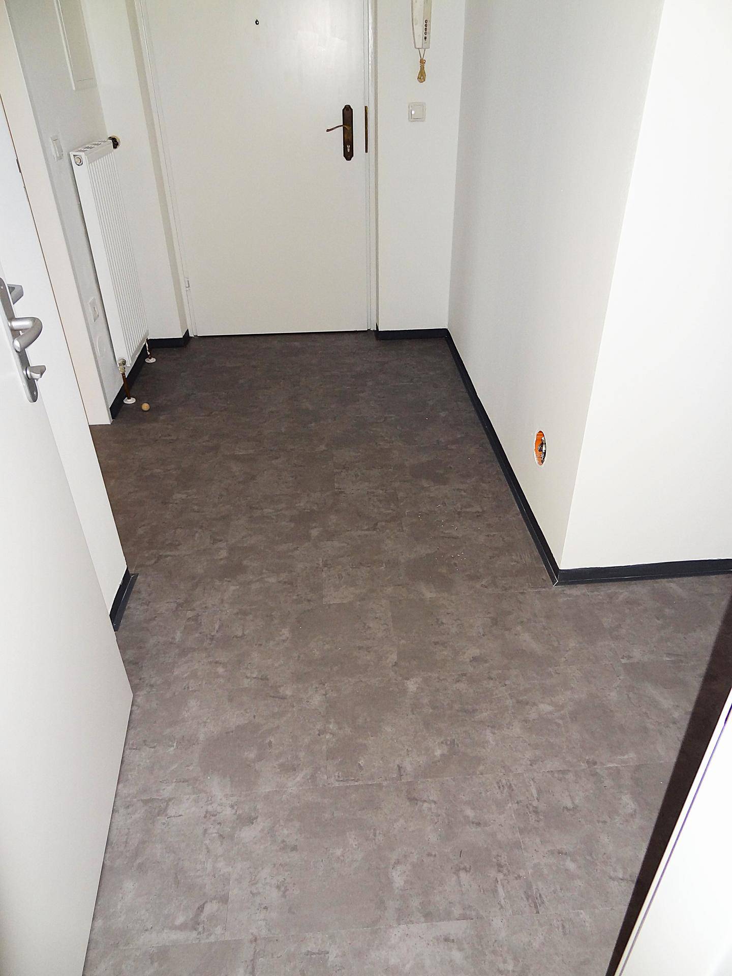 Geräumiger Eingangsbereich mit grauem Bodenbelag und weißer Wand, der einen freundlichen Empfang bietet.