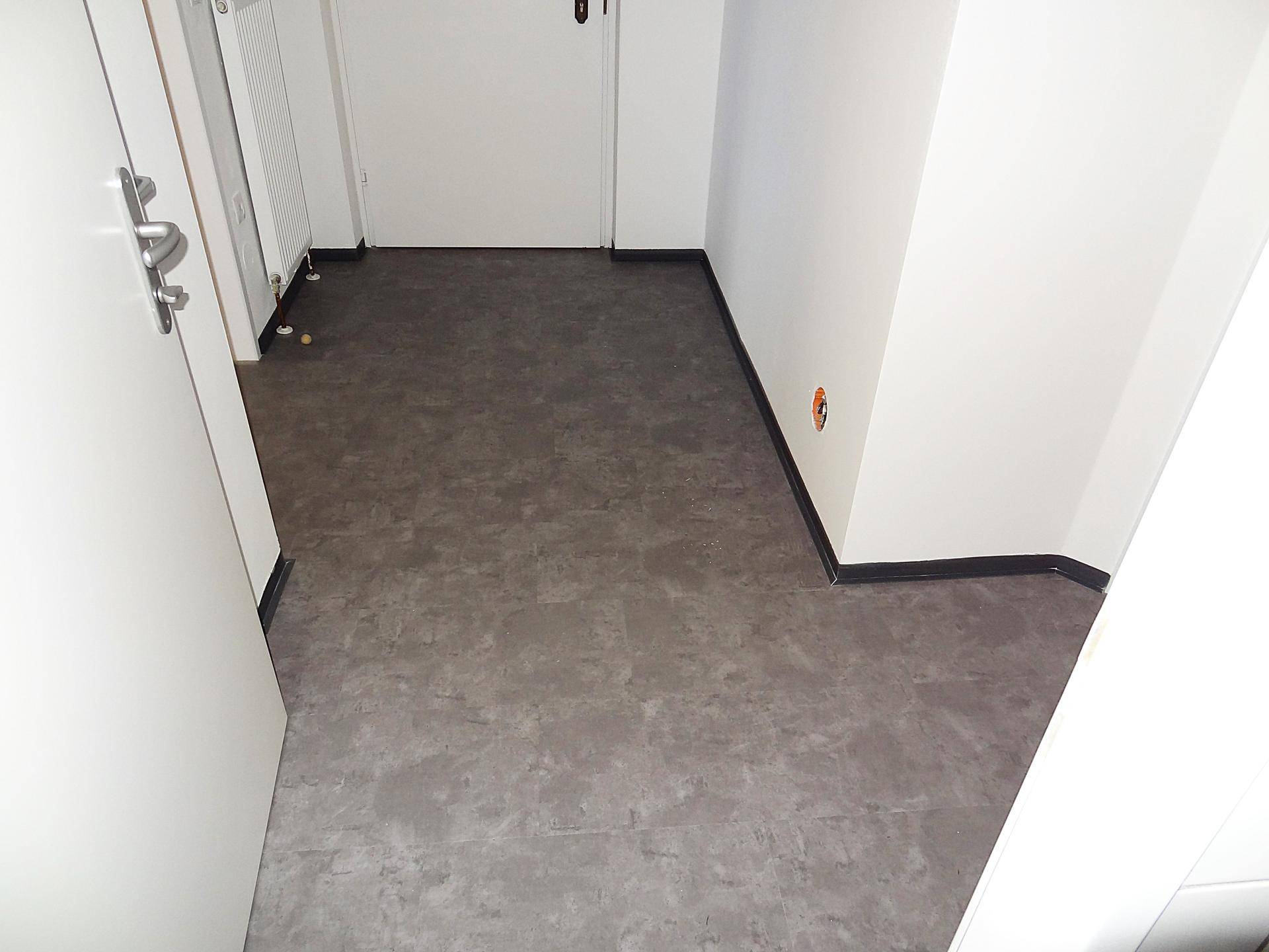 Heller Eingangsbereich mit grauem Bodenbelag und weißer Wand, der zu den Wohnräumen führt.
