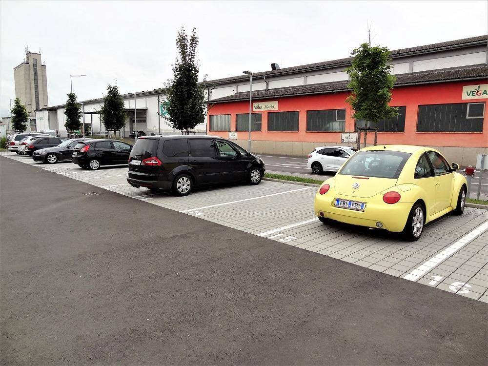 Parkplatz mit mehreren geparkten Autos, darunter ein auffälliger gelber Käfer.