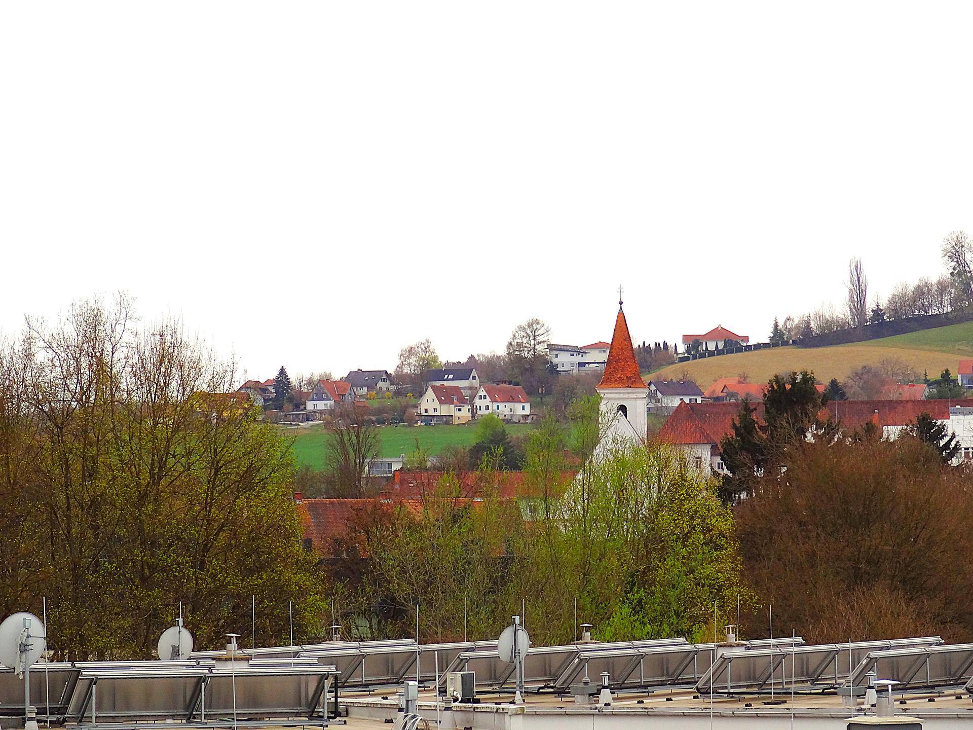 Ausblick über Dächer mit Solaranlagen, Bäume und eine Kirche in einer ländlichen Umgebung.