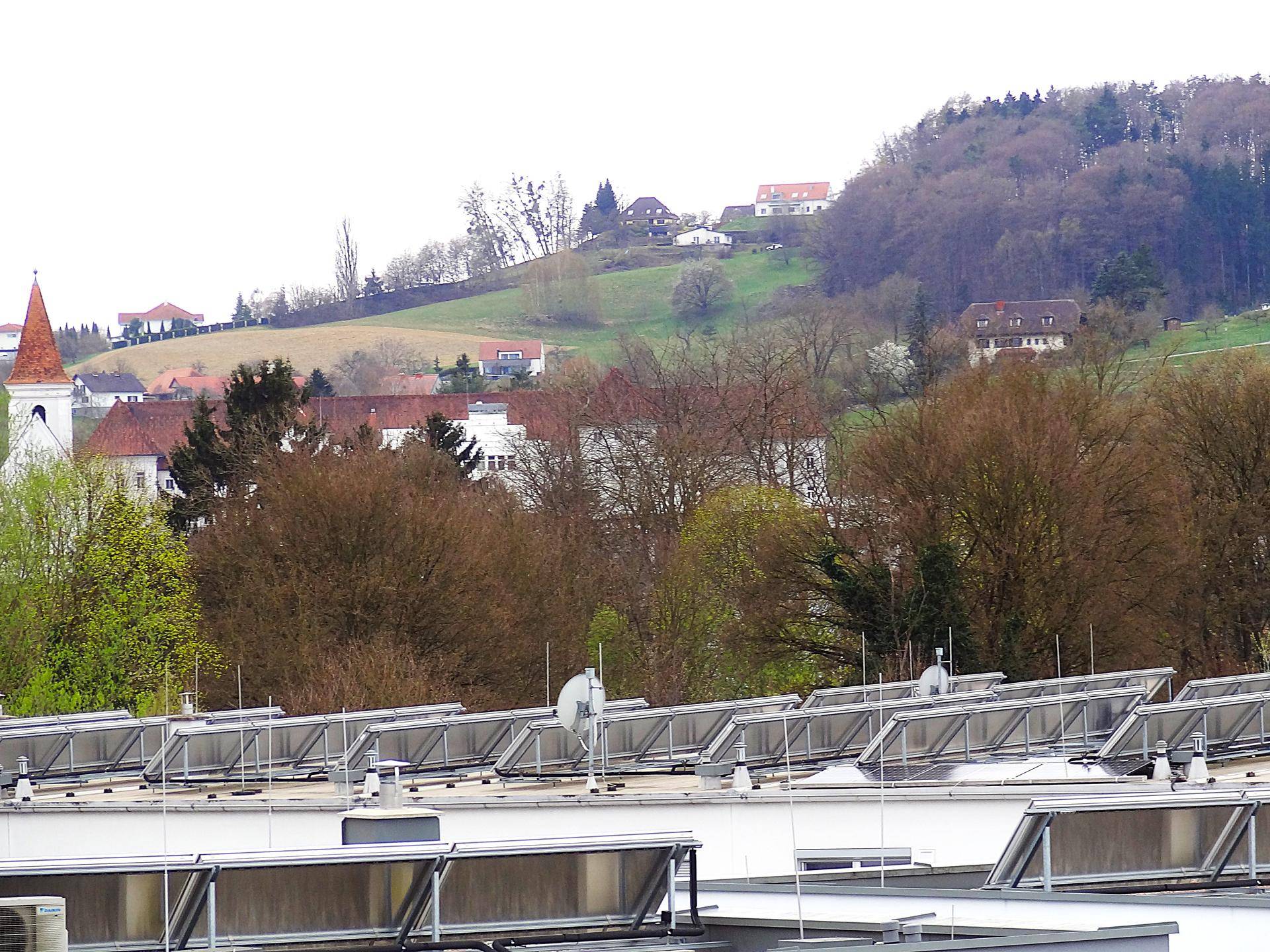 Panoramablick über Dächer mit Solaranlagen und eine hügelige Landschaft mit Häusern.