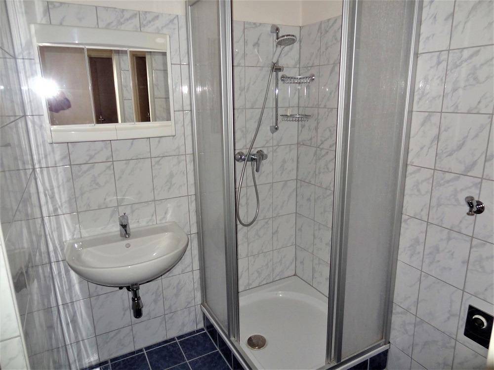 Badezimmer mit Eckdusche, Waschbecken und hellen Fliesen an Wänden und Boden.
