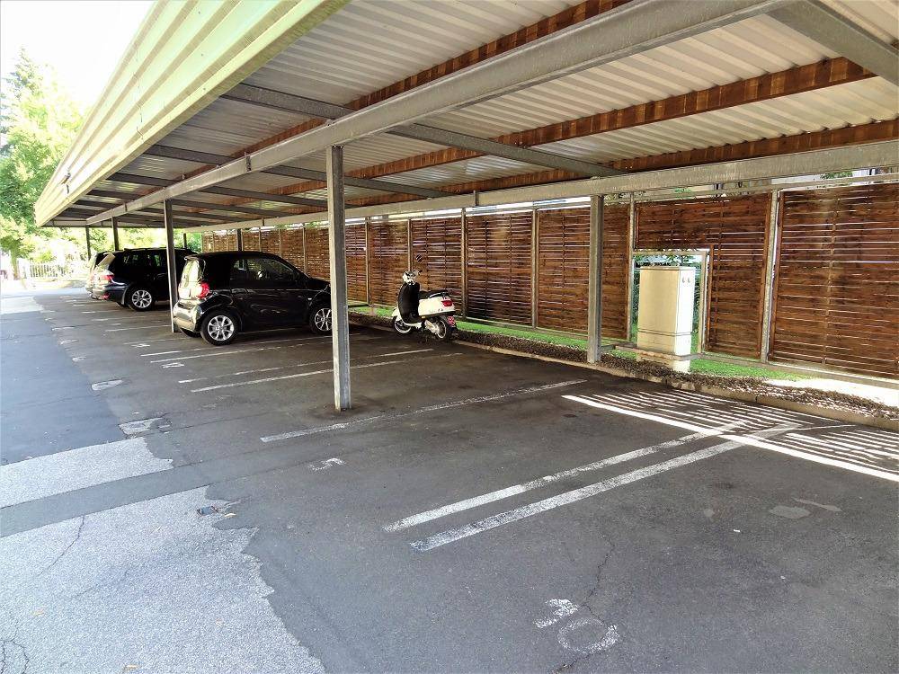 Mehrere überdachte Stellplätze in einem Carport, mit Fahrzeugen und Scooter.
