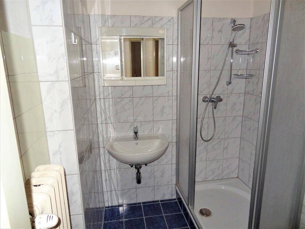 Funktionales Badezimmer mit Duschkabine, Waschbecken und Heizkörper.