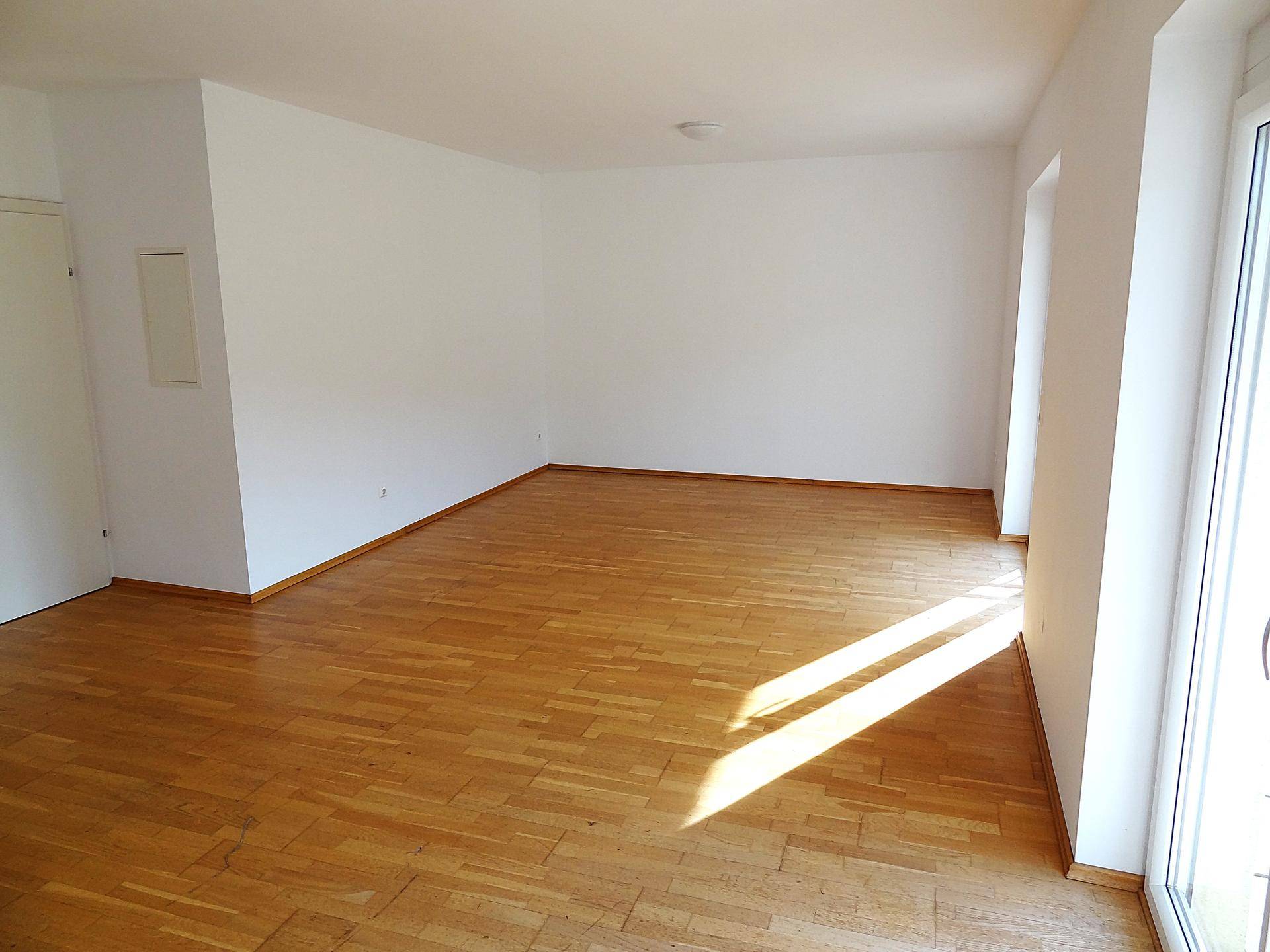 Heller Wohnbereich mit Parkettboden und Zugang zu einem Balkon, bietet eine angenehme Atmosphäre und viel Tageslicht.