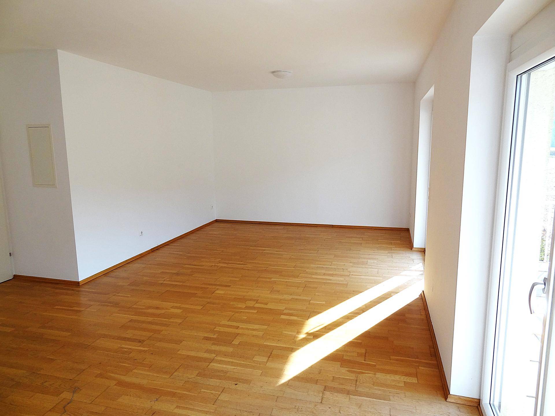 Geräumiger Wohnbereich mit hellem Parkettboden und großzügigem Zugang zum Außenbereich, ideal für sonnige Tage.