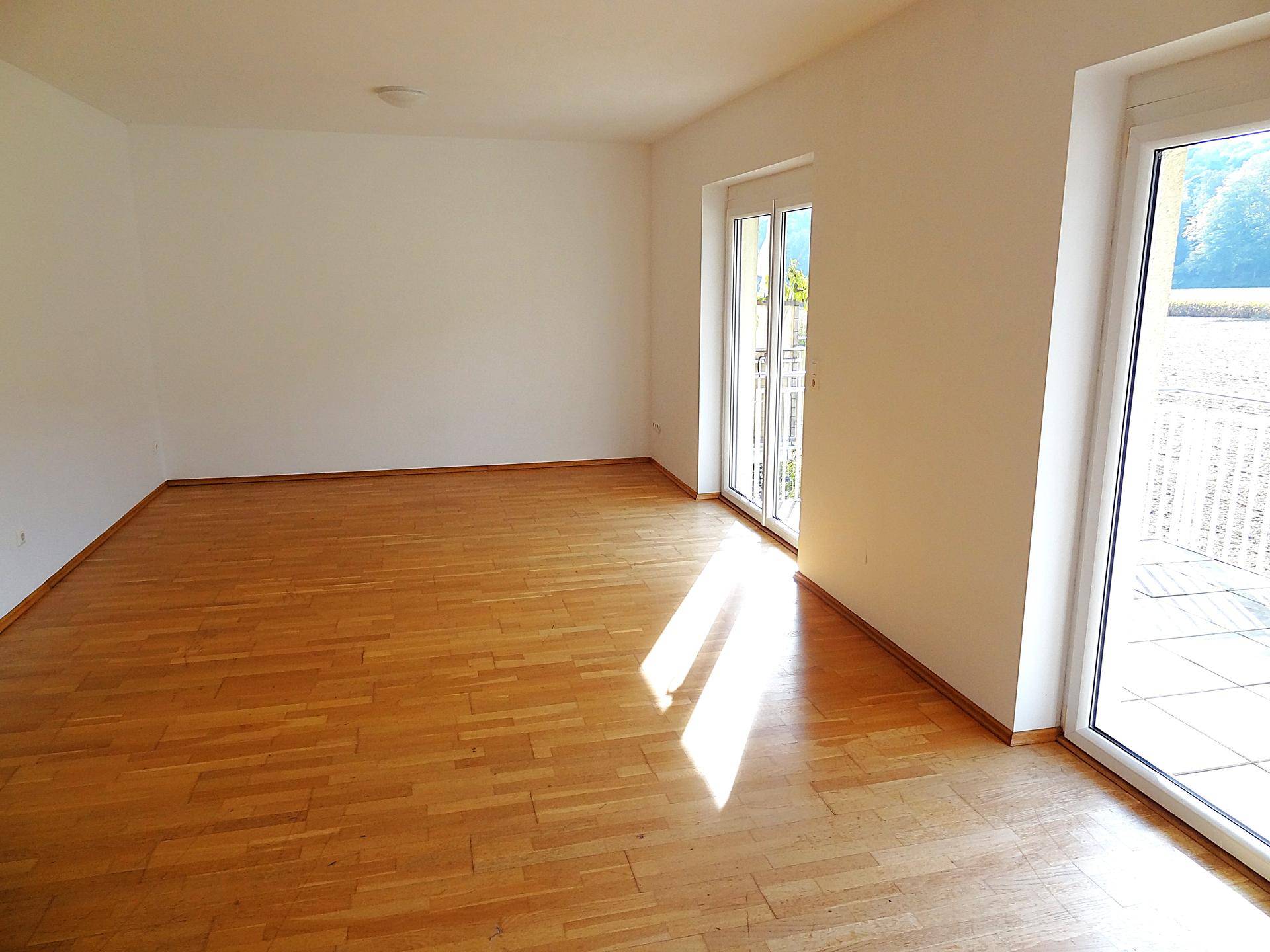Heller Wohnraum mit Parkettboden und zwei großen Fenstern, die einen schönen Ausblick auf die Landschaft bieten.
