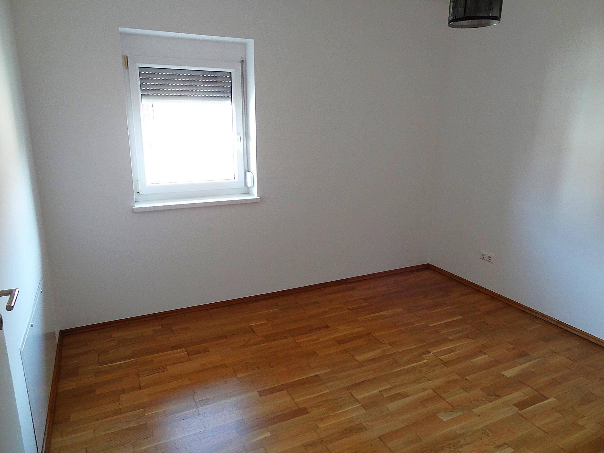 Helles Schlafzimmer mit Parkettboden und Fenster mit Rollladen, bietet eine ruhige und private Atmosphäre.