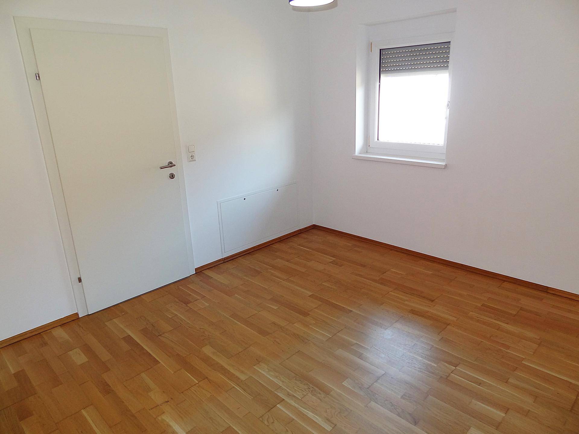 Heller Raum mit Parkettboden, weißer Tür und Fenster mit Rollladen, bietet vielseitige Gestaltungsmöglichkeiten.