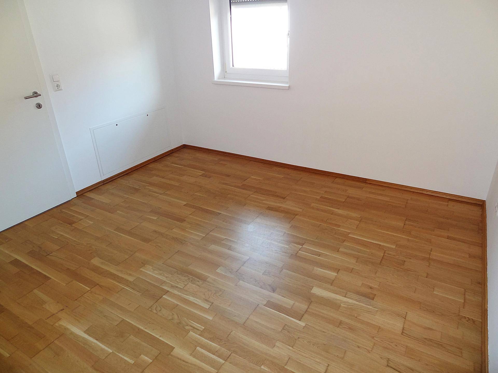 Geräumiger Raum mit Parkettboden und einem Fenster, das viel Tageslicht hereinlässt.