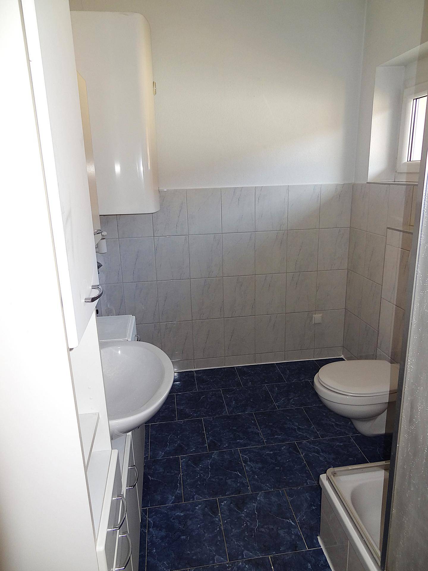 Helles Badezimmer mit blauen Bodenfliesen, weißem Waschtisch und einer praktischen Duschkabine.