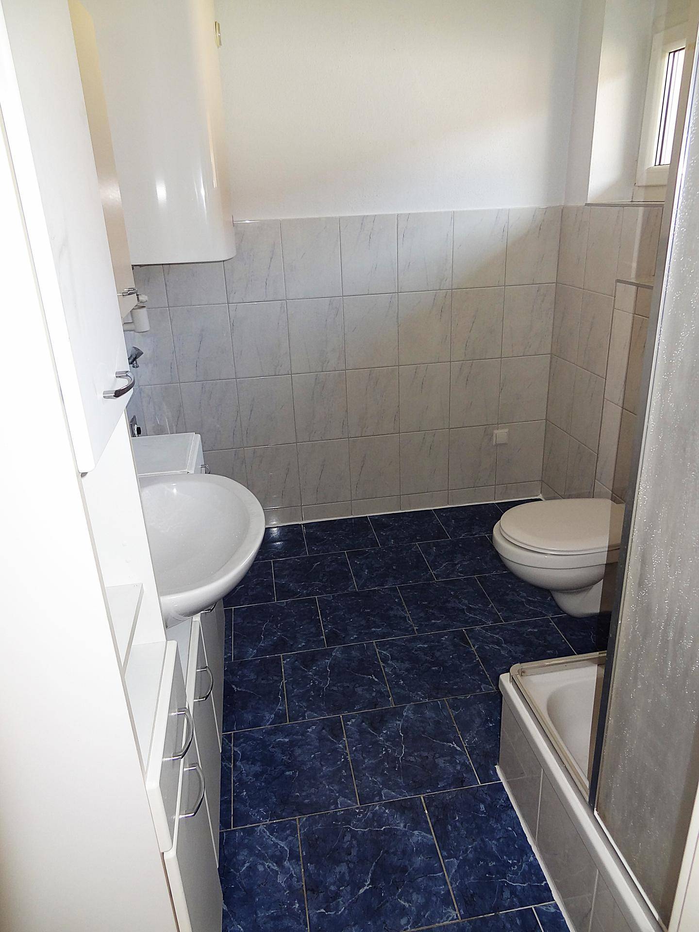 Badezimmer mit blauen Fliesen, weißer Keramik und einem Warmwasserboiler, gut gepflegt.