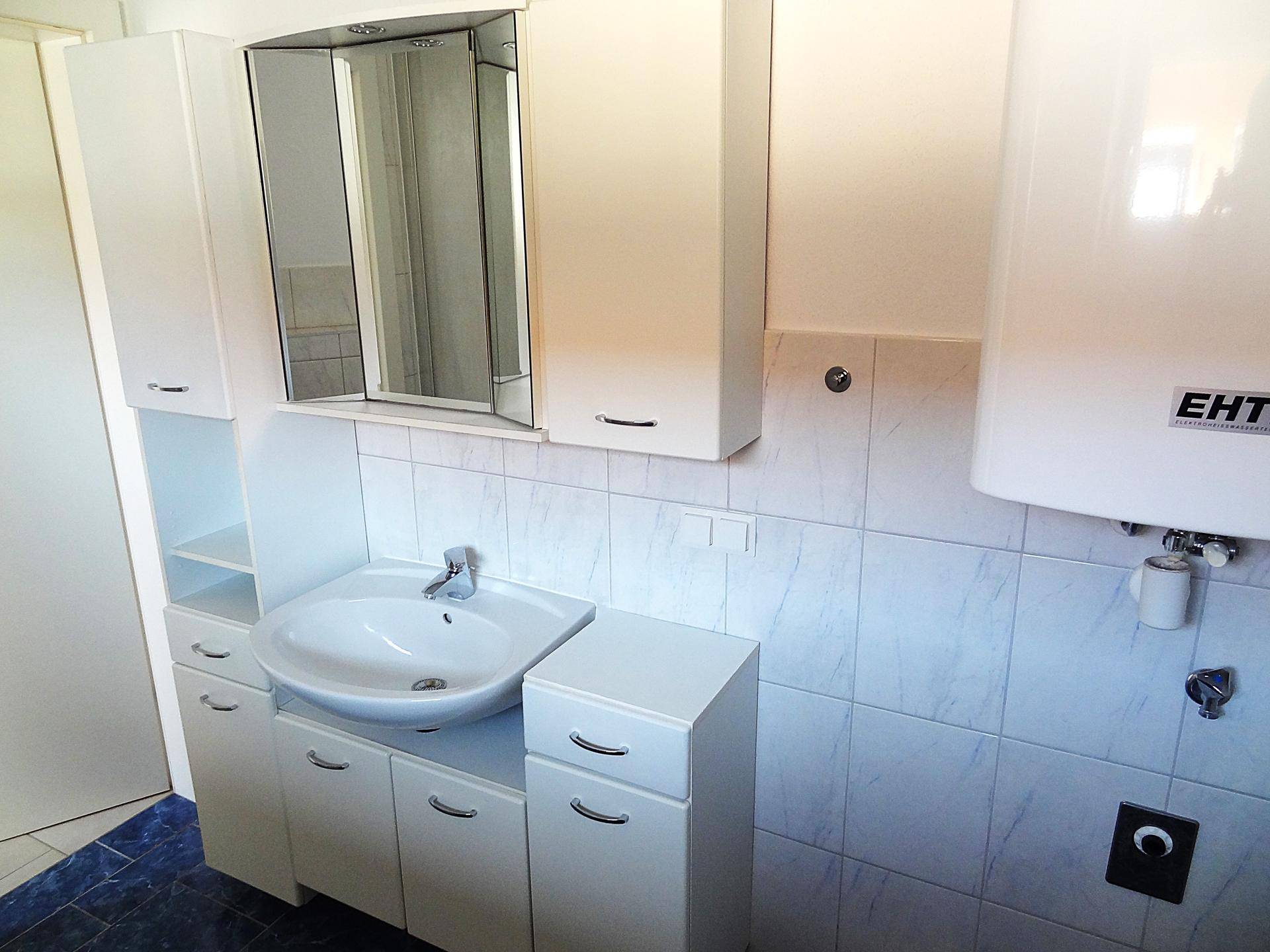 Waschtischbereich mit Waschbecken, Spiegelschrank und Unterschränken, daneben ein Warmwasserboiler.