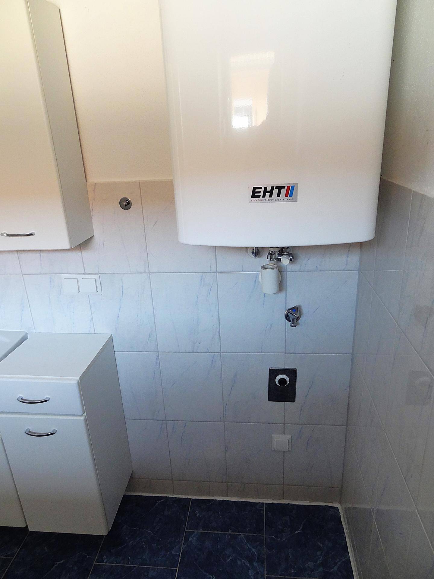 Detailansicht des Warmwasserboilers und der hellen Wandfliesen im Badezimmer.