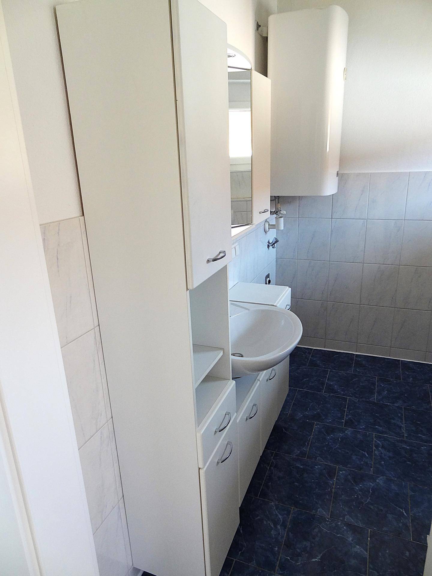 Badezimmer mit Waschtisch, hohen Schränken und Warmwasserboiler, bietet viel Stauraum.