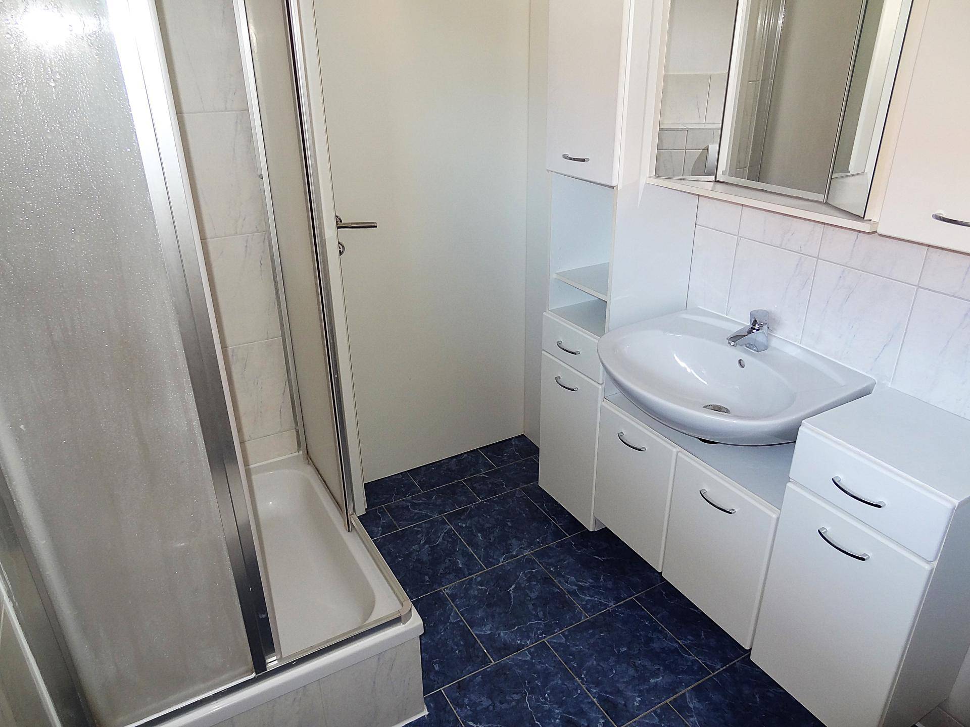 Geräumiges Badezimmer mit Duschkabine, Waschtisch und WC, alles in hellen Farben gehalten.
