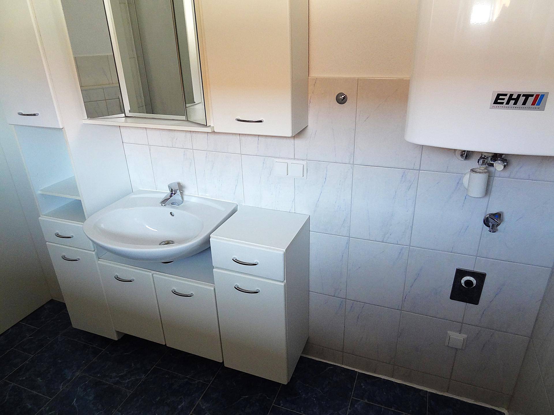 Waschtisch mit Waschbecken, Spiegelschrank und Boiler im Badezimmer, bietet Komfort und Stauraum.