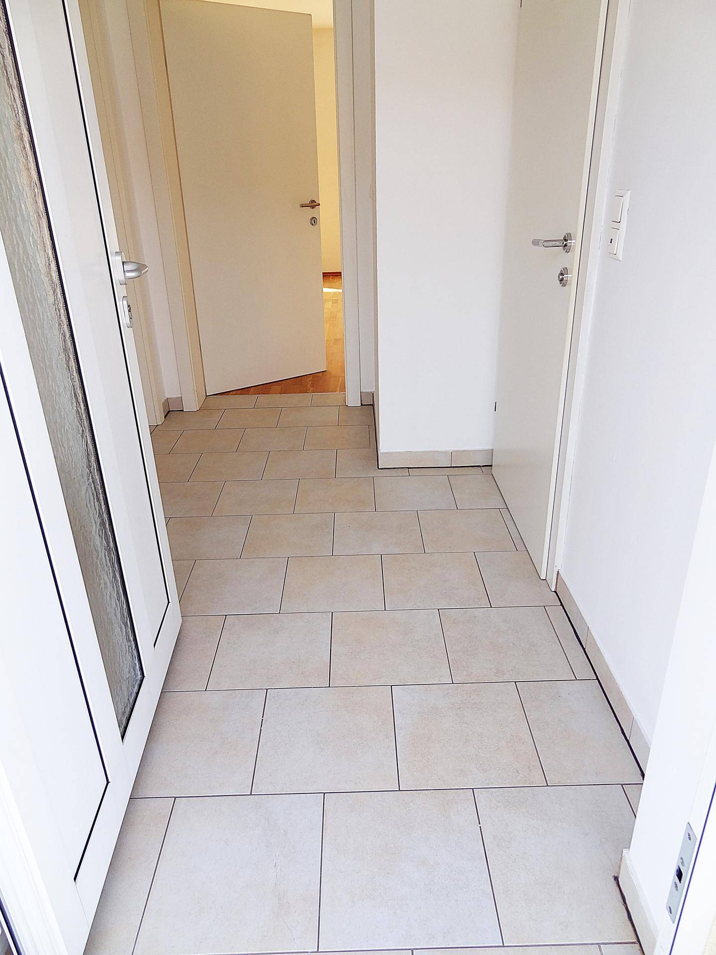 Einladender Flur mit hellen Bodenfliesen und offener Tür, die den Zugang zum Haus ermöglicht.