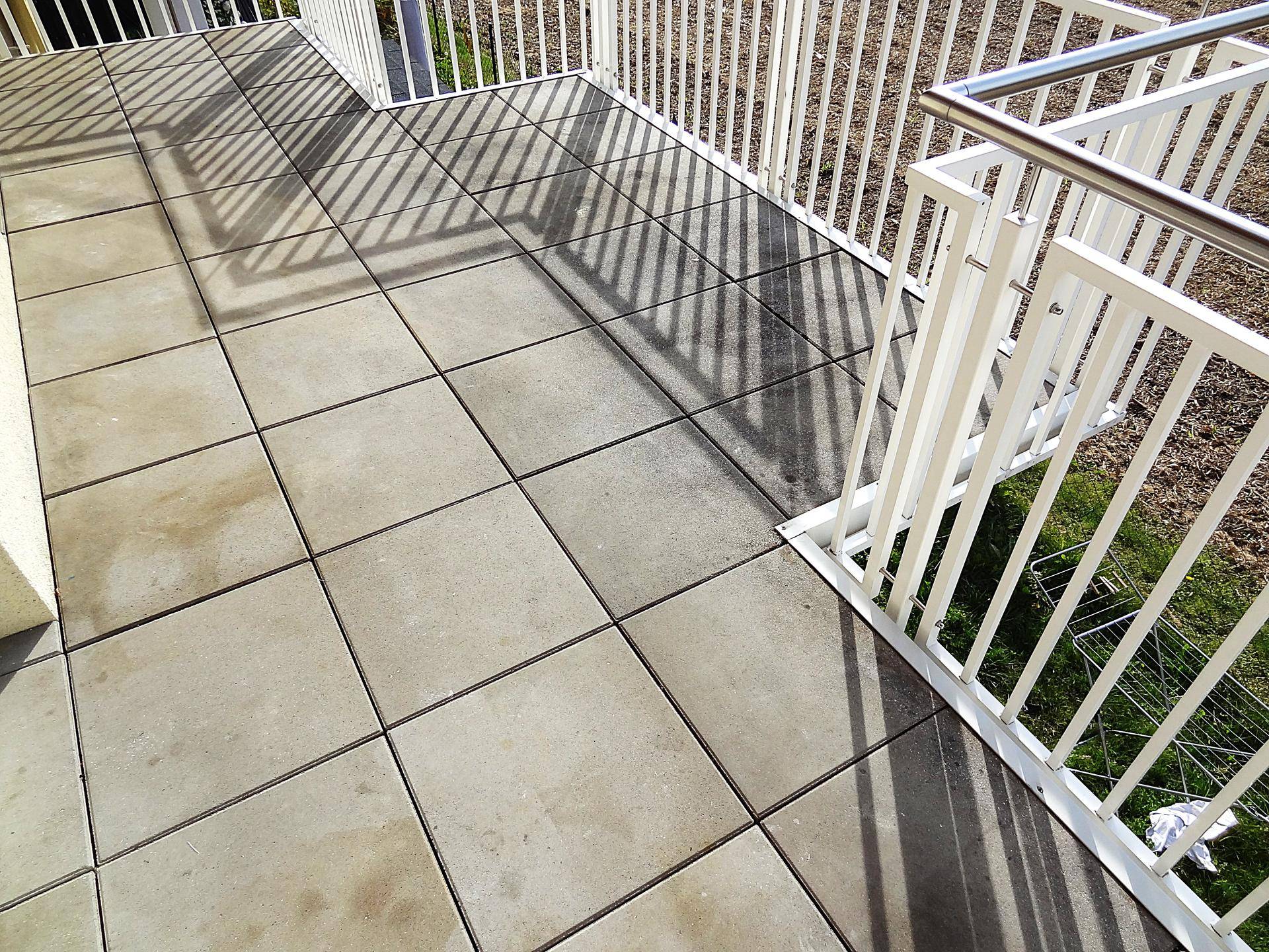 Heller Balkon mit grauen Fliesen und weißem Geländer, ideal für sonnige Stunden im Freien.